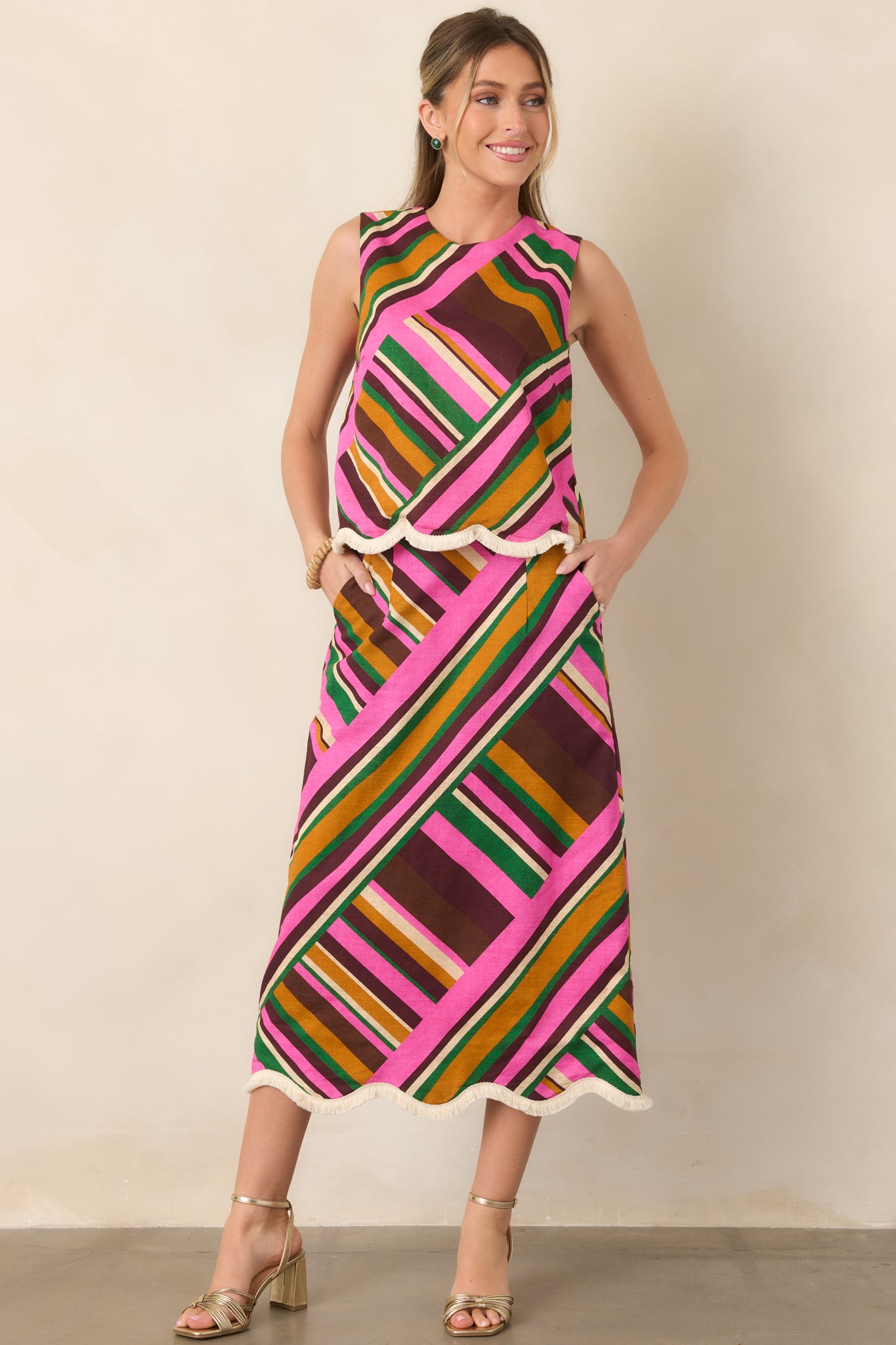 Pink multi geometric stripe midi skirt with a high-rise waistband, softly flared shape, side pockets, and scalloped fringe-trim hem.
