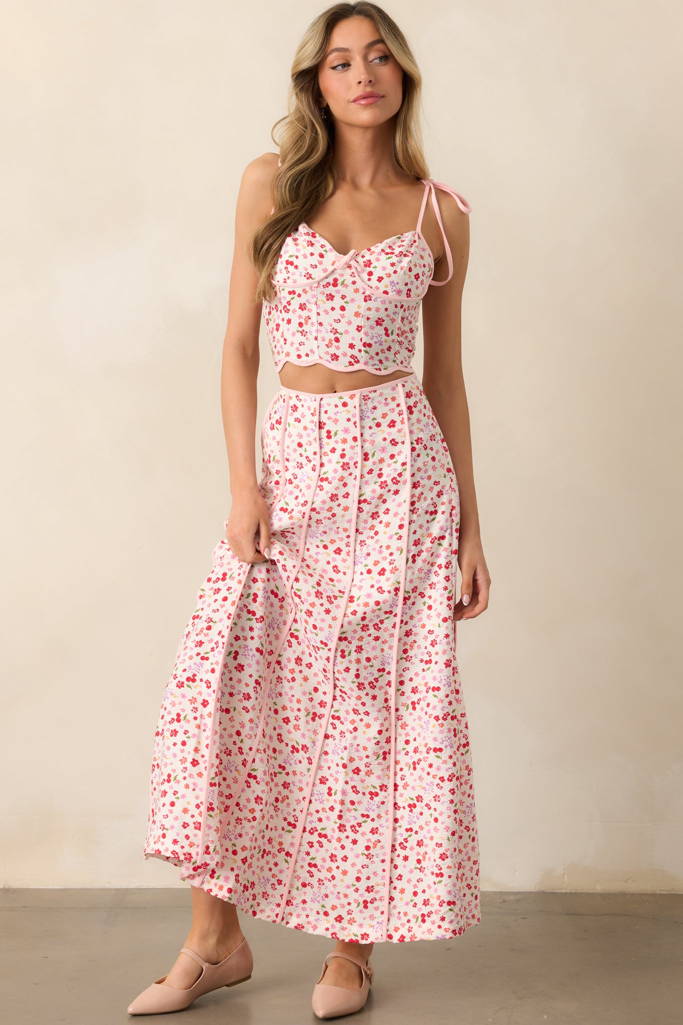 This feminine pink top combines a multicolor floral and cherry print with adjustable self-tie bows at the bust and a scalloped hem for added style and shape.