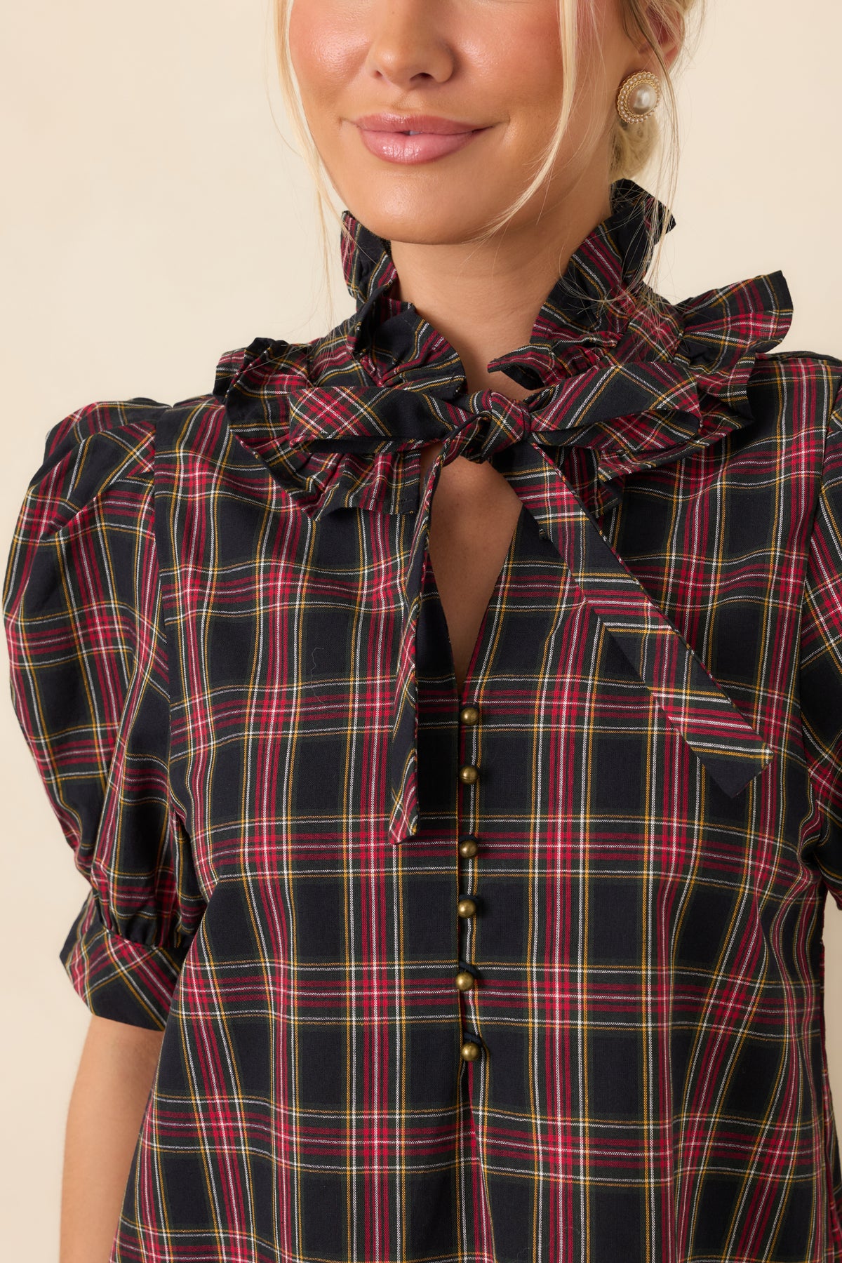 Close detail of the ruffled stand collar, plaid bow tie, and small round front buttons.
