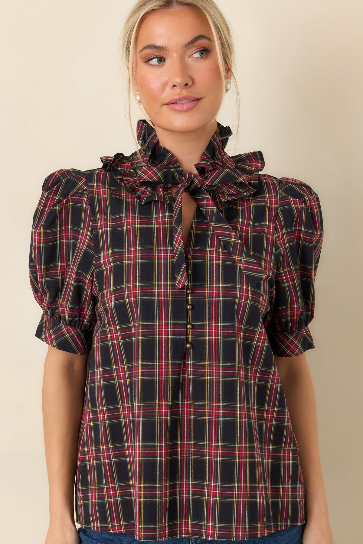 Small round buttons accent the front opening beneath the plaid blouse's tied neckline.