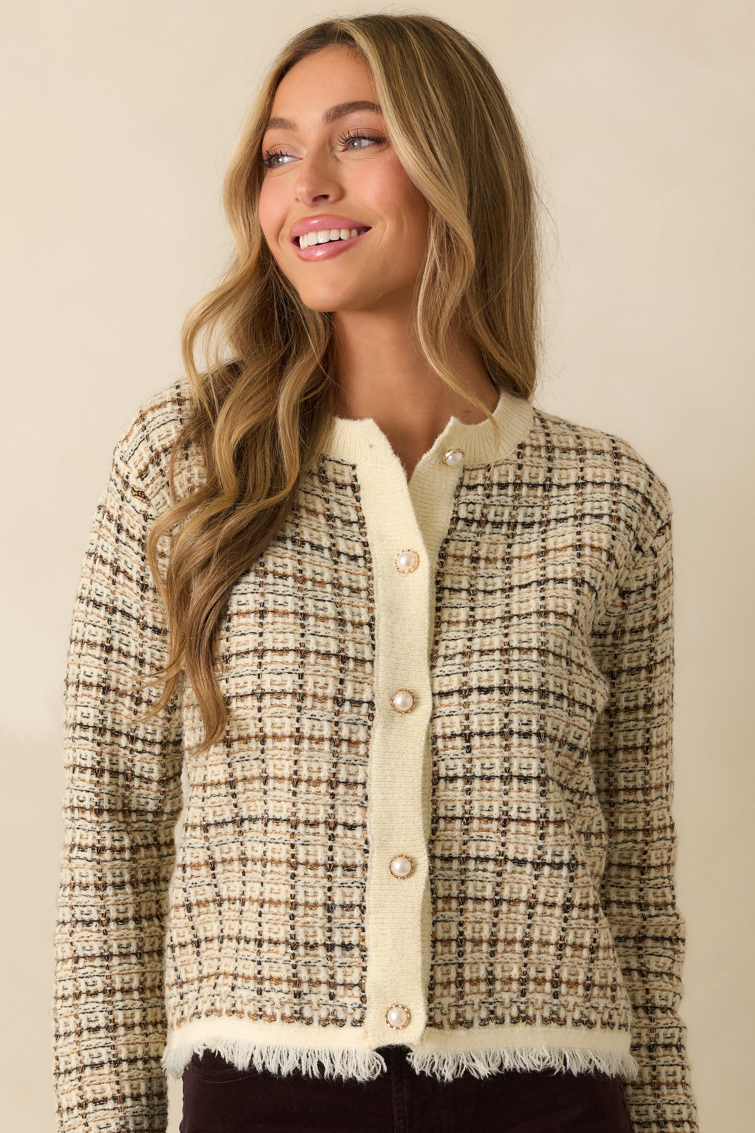 Detail of long sleeve and button closure on plaid knit cardigan, highlighting golden threads and fringe hem.