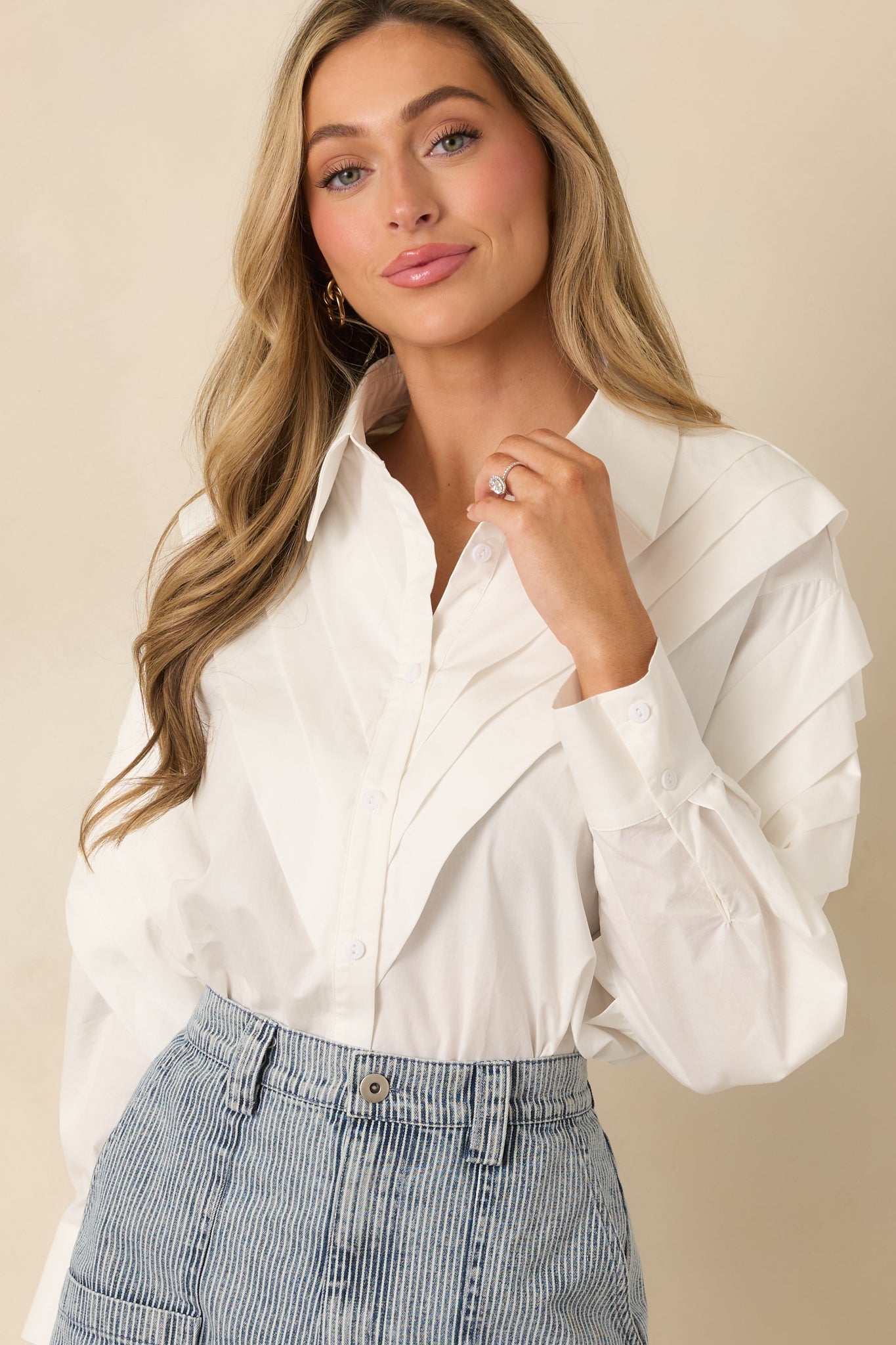 Pleated shoulder detailing on a white woven cotton button-up blouse with a smooth, lightweight texture.