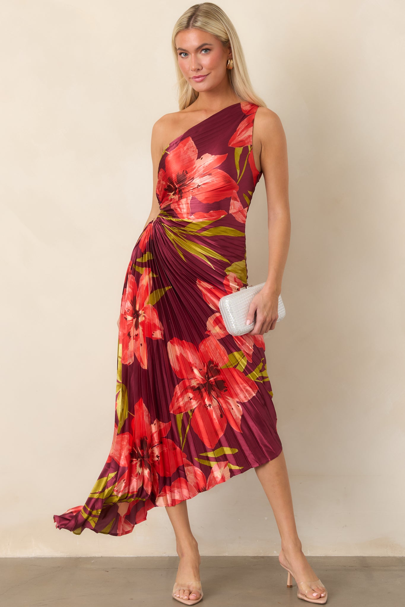 Plum satin dress featuring a bold coral and olive hibiscus print, one-shoulder neckline, pleated construction, and asymmetrical high-low hem.