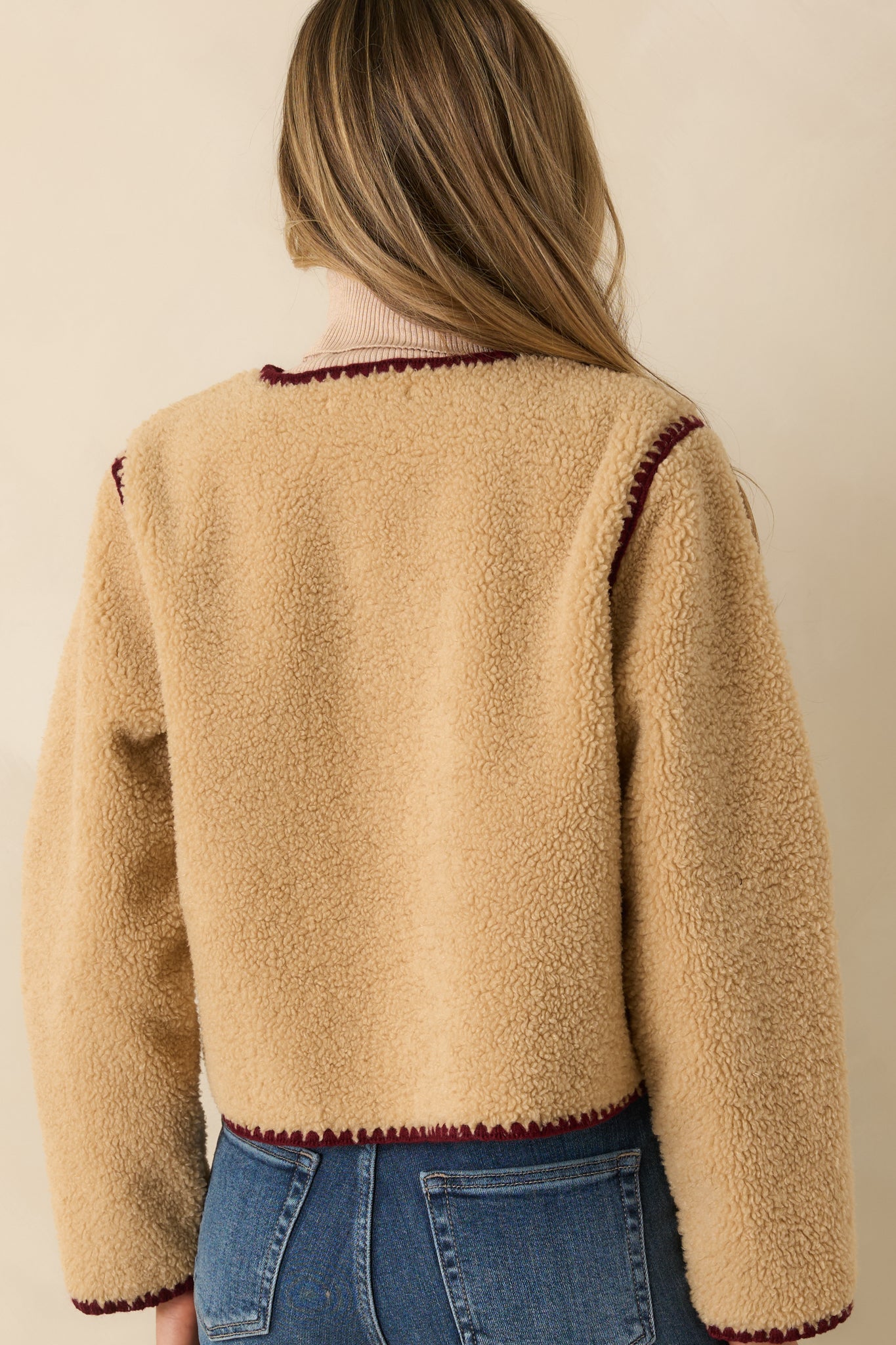 Plush beige sherpa jacket with relaxed silhouette and burgundy-trimmed edging along the rear.