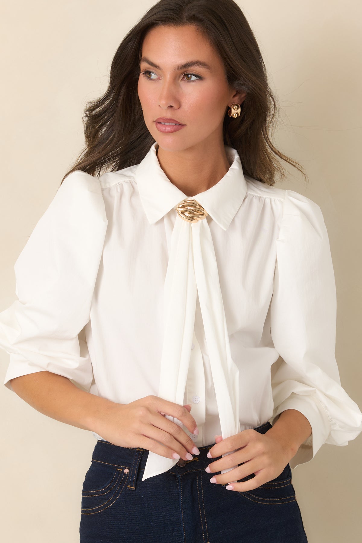 Pointed collar framing draped neck ties gathered beneath a sculptural gold-tone accent.