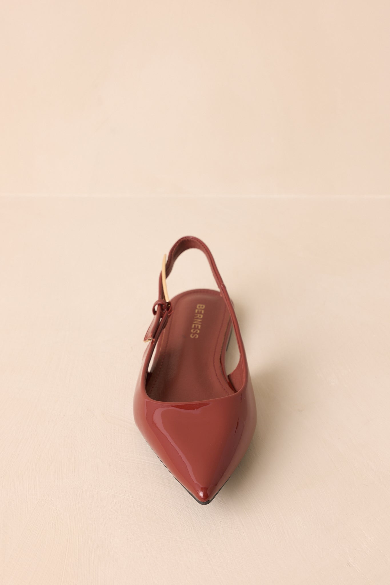 Copper brown pointed-toe flats resting against a beige backdrop with glossy sheen.