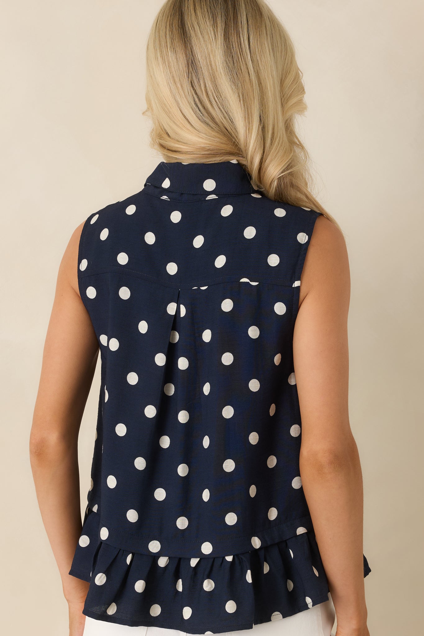 Rear view of the sleeveless polka dot blouse highlighting the relaxed silhouette, smooth lining, and flowing ruffled hem.