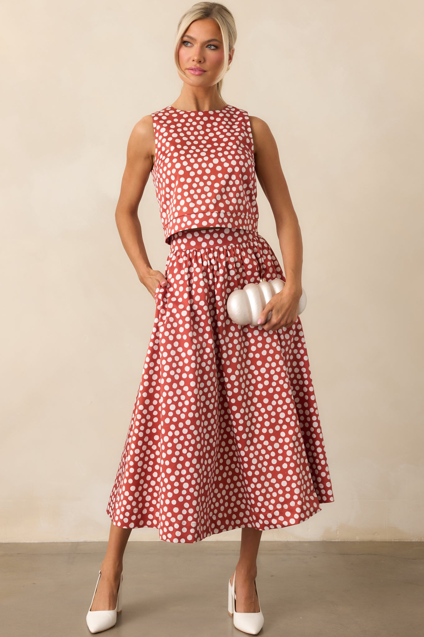 Brick red sleeveless top with ivory polka dots and a structured cropped silhouette.