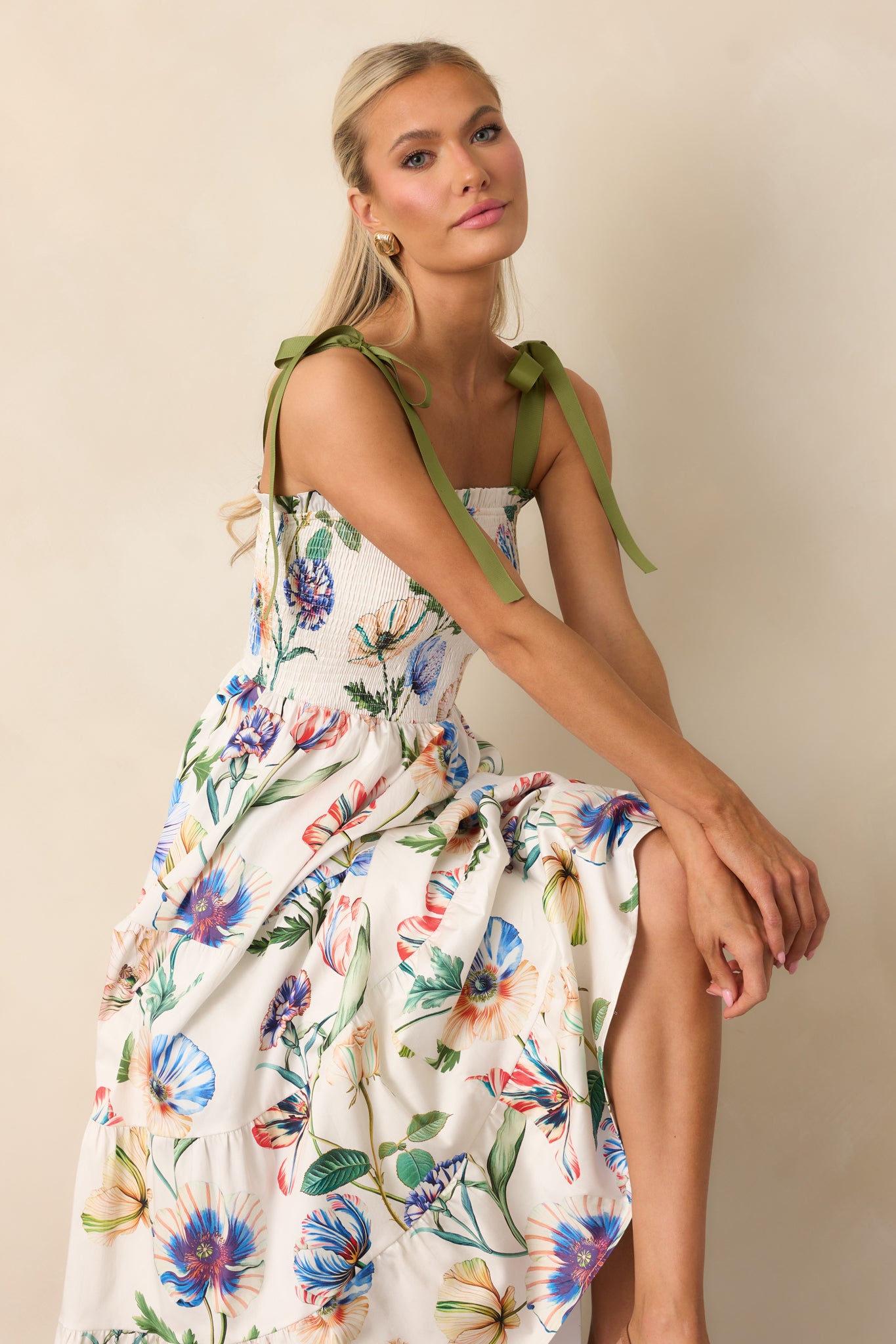 Ivory midi dress with multicolor floral print, green adjustable bow straps, and square neckline with ruffle trim.
