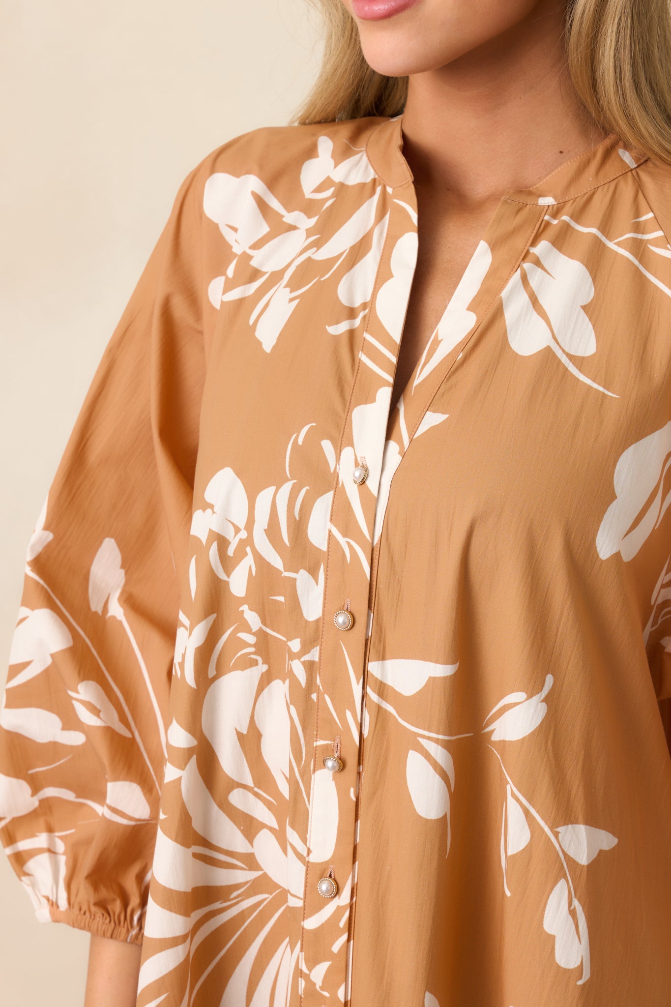 Detailed view of the fawn brown and ivory floral print, notch v-neckline, and button front closure.