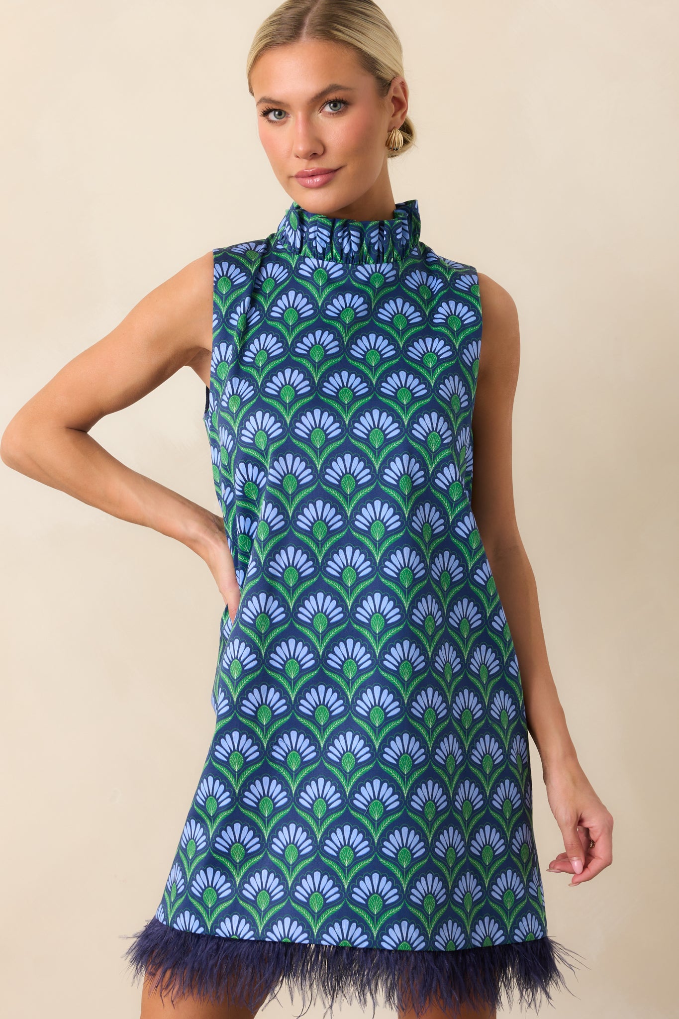 Blue multicolor geometric print mini dress styled to showcase the shift silhouette, feather-trimmed hem, and sleeveless design.