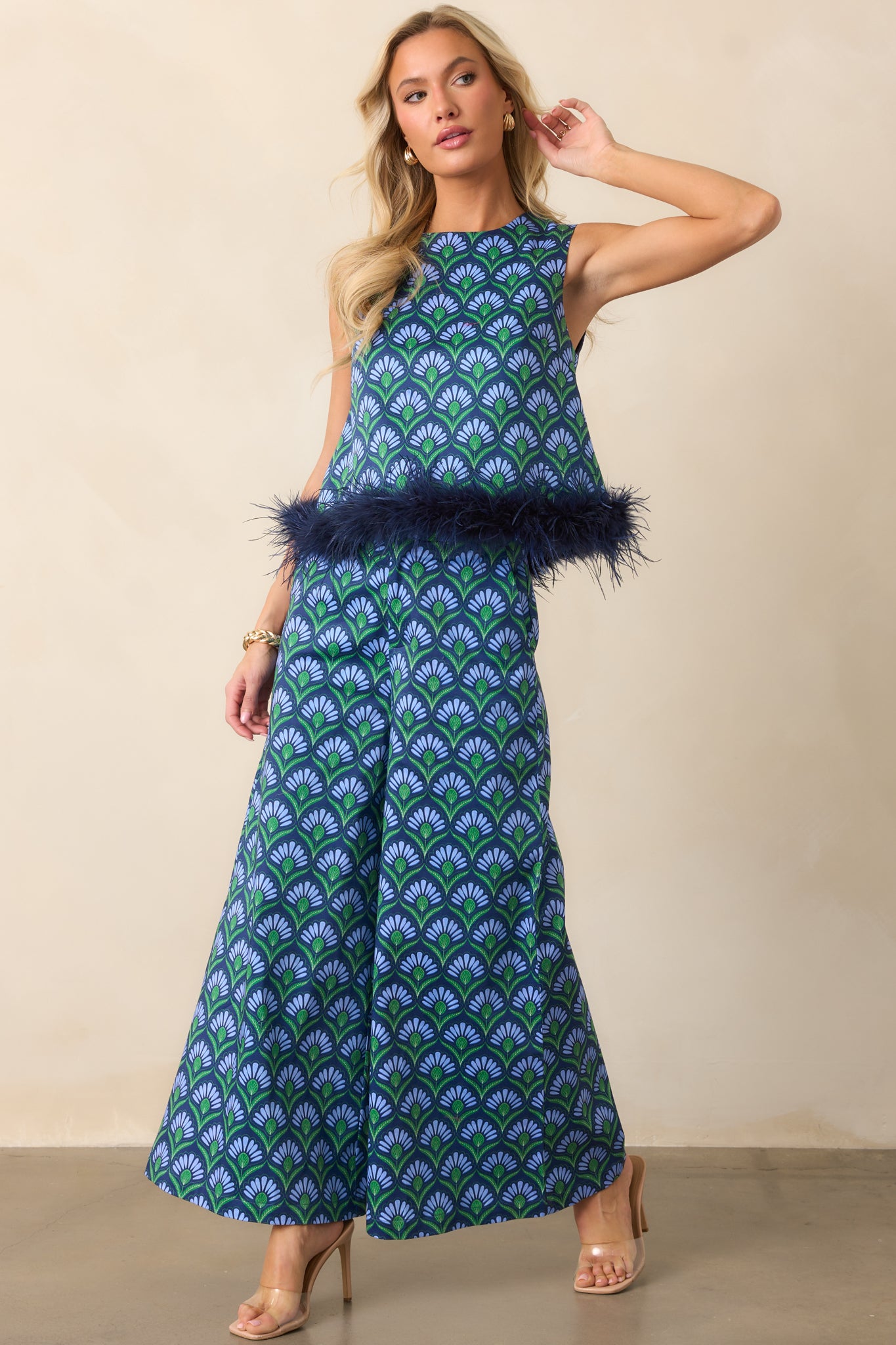 Front view of high-rise pants with a blue multicolor geometric pattern, wide leg silhouette, functional side pockets, and ivory faux pearl button closure.