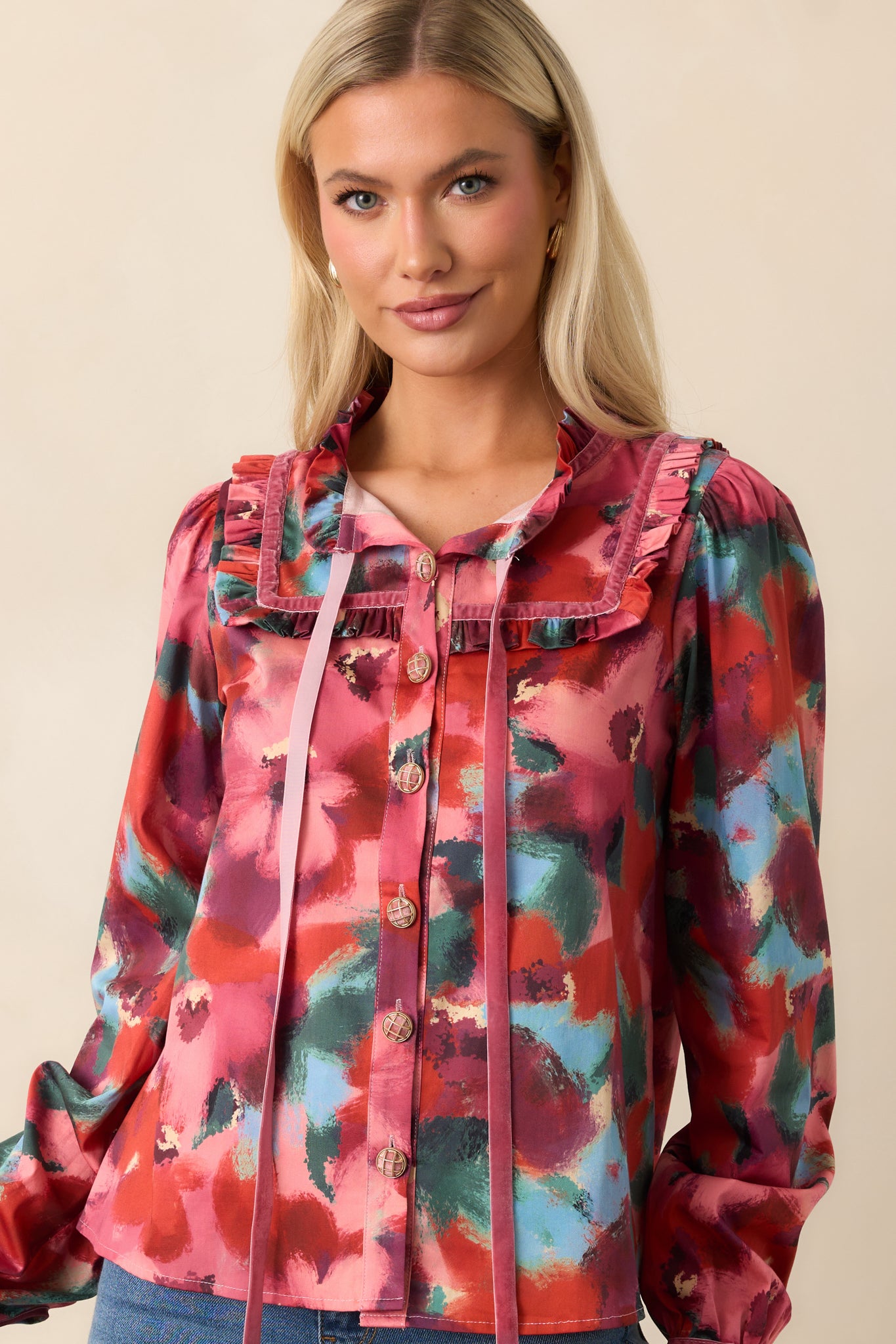 Close crop of the pink top’s V-neckline with long ribbon tassels and ruffle-trimmed sailor collar over multicolor floral print.