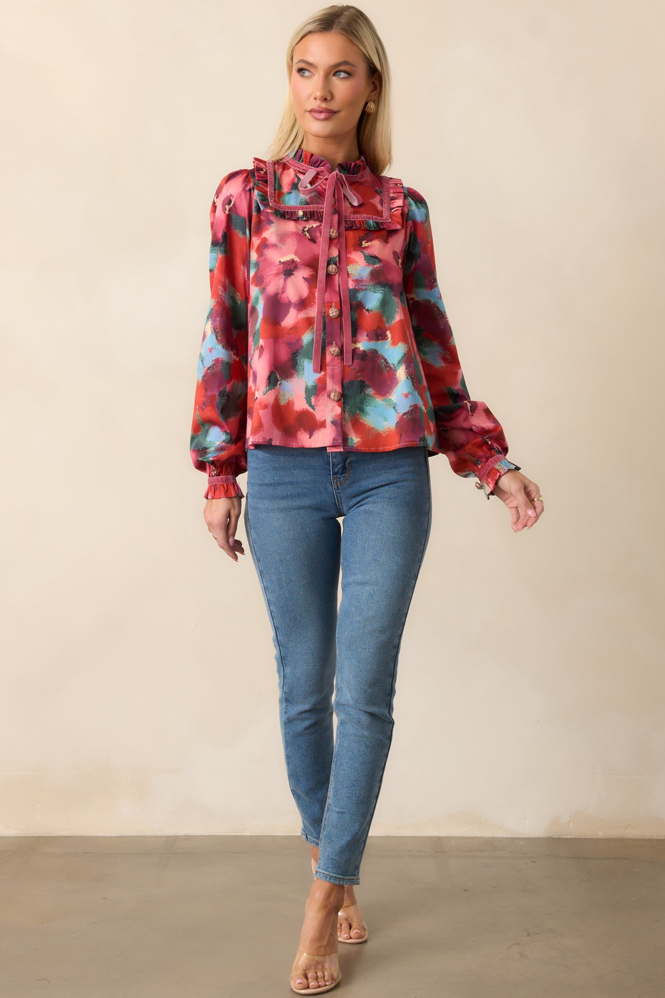 Full-length view of a floral-printed pink top with sailor-inspired ruffle collar, self-tie tassels at the neckline, and long sleeves with buttoned ruffle cuffs.