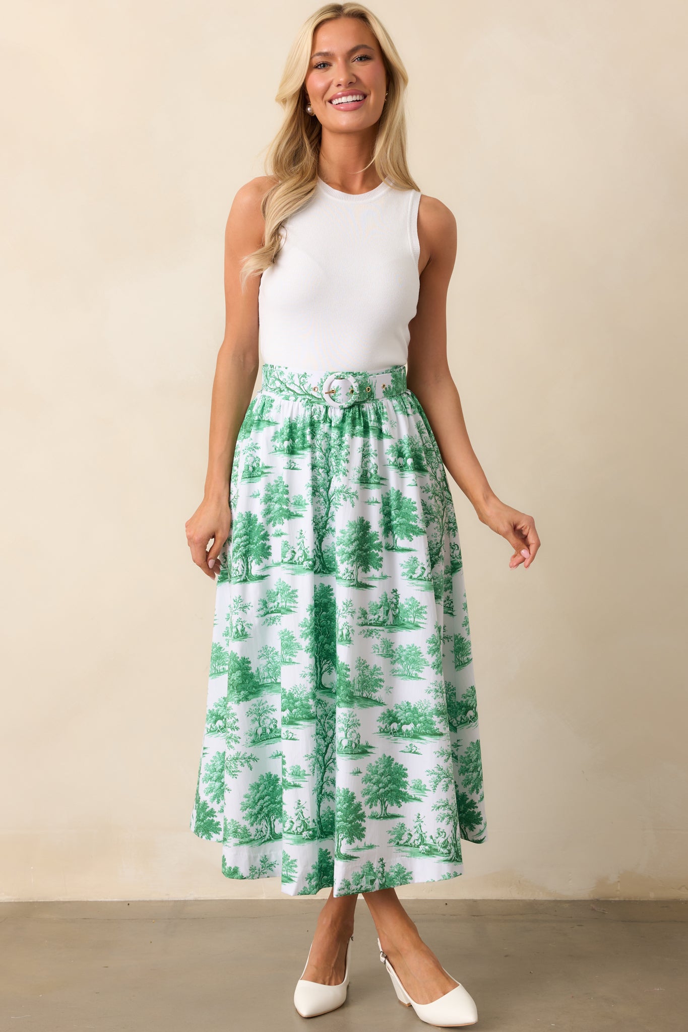 This eden green midi skirt is adorned with a charming toile print, complete with belt loops, a matching adjustable belt, and functional pockets for a stylish, practical design.