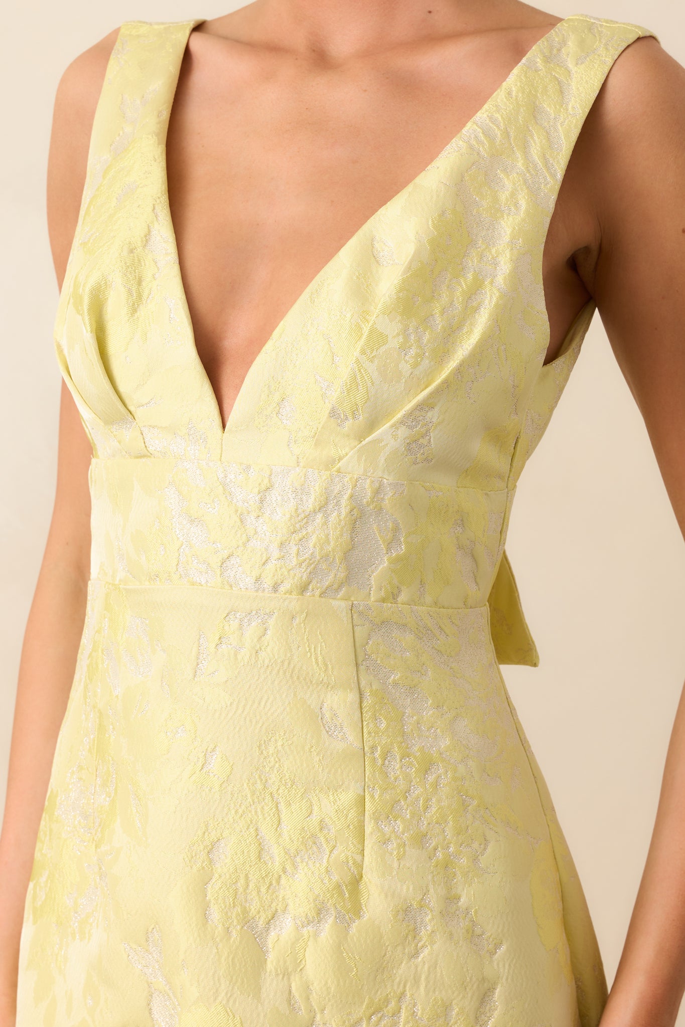 Close-up of gold detailing and fabric texture on a yellow mini dress with v-neckline.