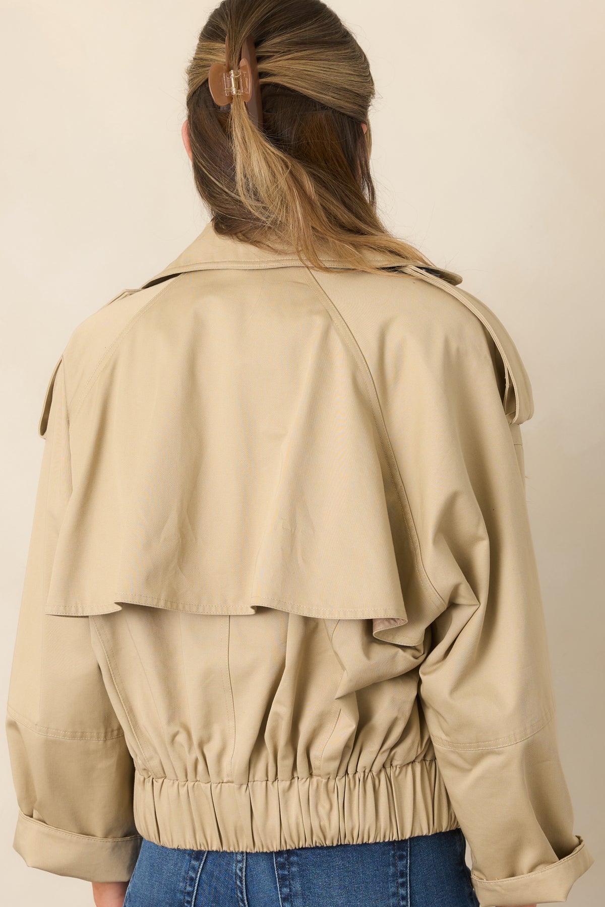 The rear of the beige cropped trench jacket features an adjustable storm flap and elasticized waist.