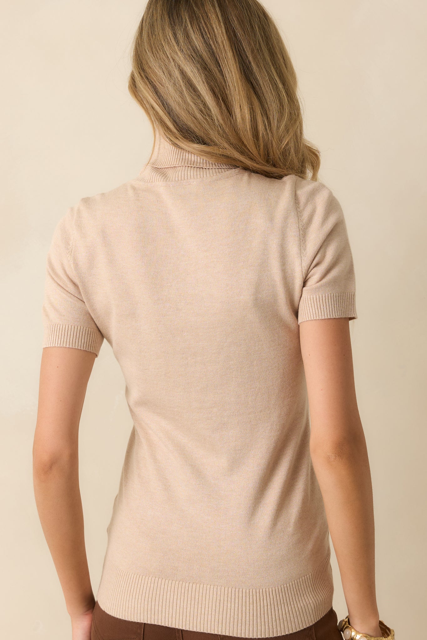 Rear view of the beige sweater showing short sleeves, ribbed hems, and slightly fitted silhouette.