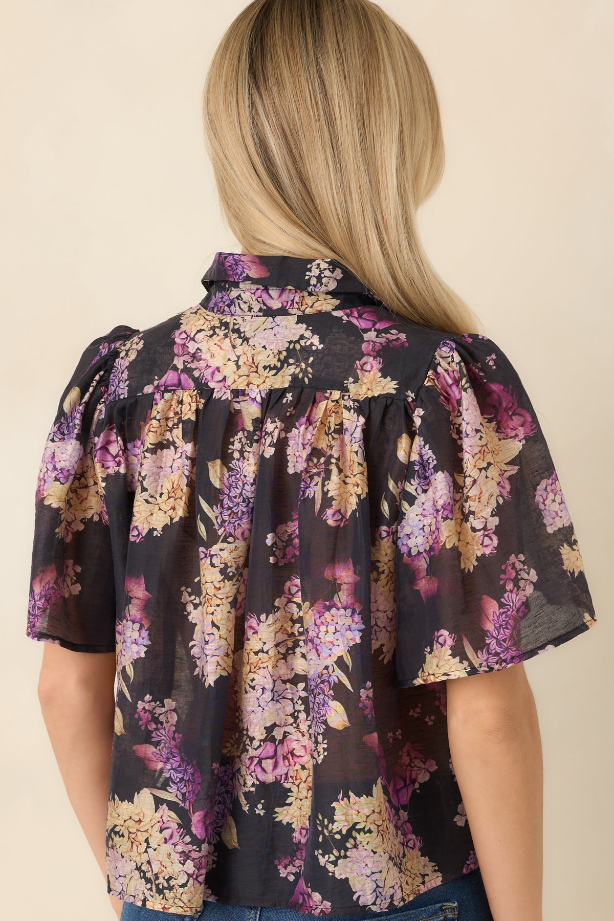 Rear of the black floral blouse showing the gathered back yoke, flutter sleeves, and scattered multicolor blooms.