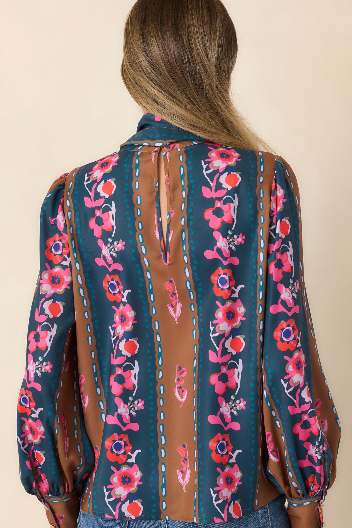 Rear view of the blue and caramel striped floral blouse featuring a back keyhole, gathered shoulders, and long sleeves.