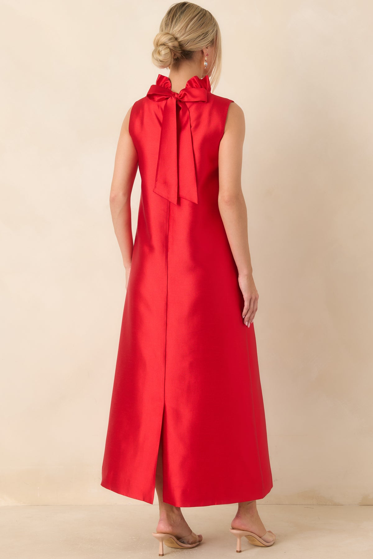 Rear view of the bright red sleeveless maxi dress featuring a back bow tie detail and a flowing floor-length silhouette.