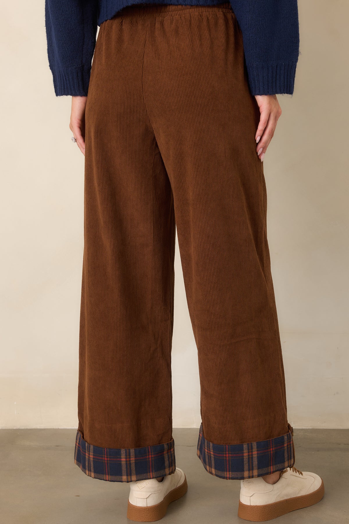 Rear of the brown wide-leg pants showing the relaxed silhouette, drawstring waistband, and navy plaid cuffs.