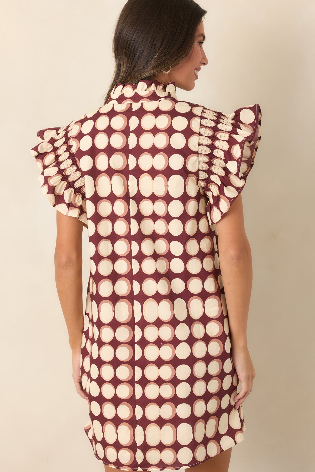 Rear view of the burgundy cotton mini dress showing the oversized ivory dot pattern, relaxed shift silhouette, short flutter sleeves, and loose hemline.