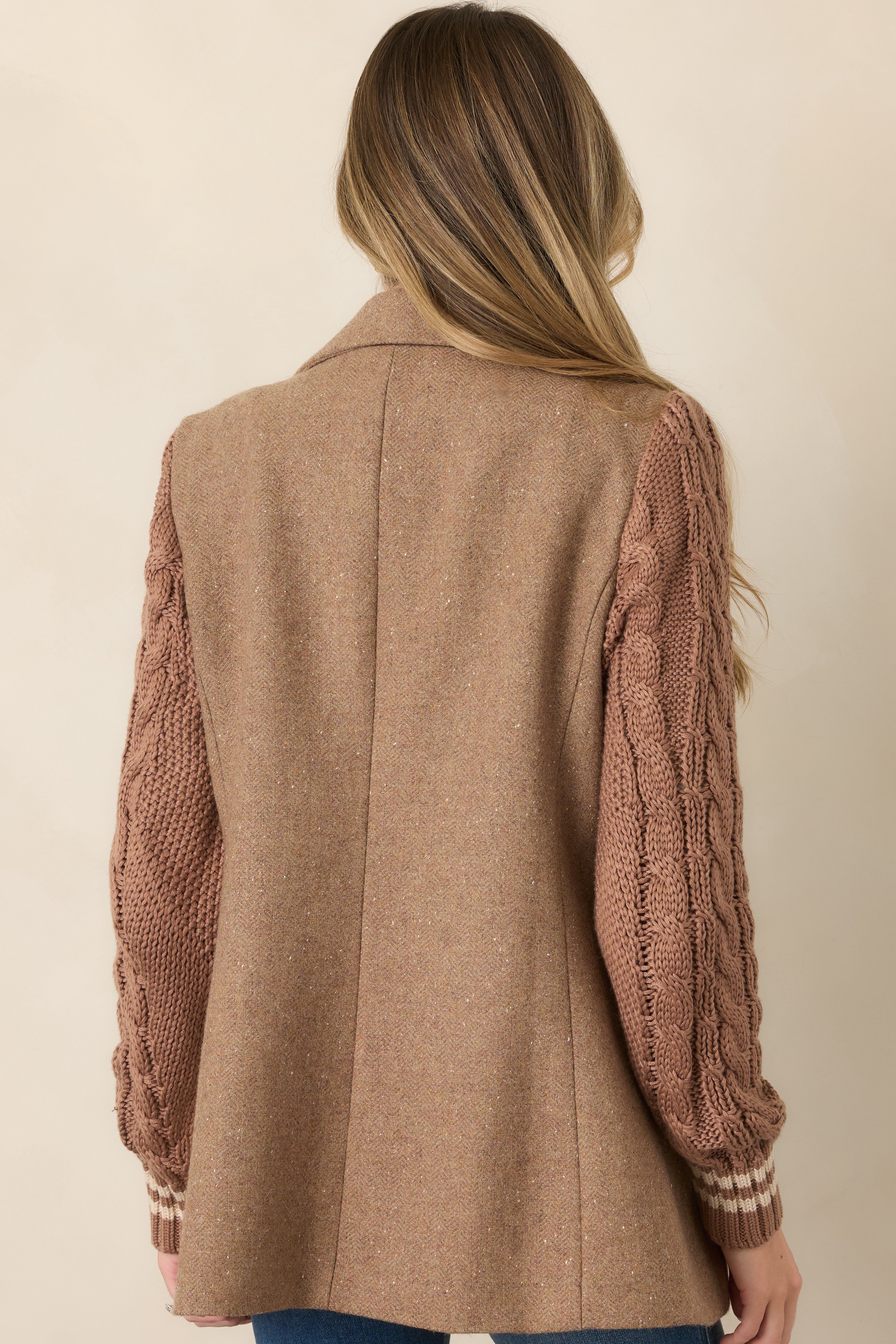 Rear view of the camel wool-blend blazer featuring a structured mid-thigh silhouette and contrasting cable-knit sleeves with ribbed cuffs.
