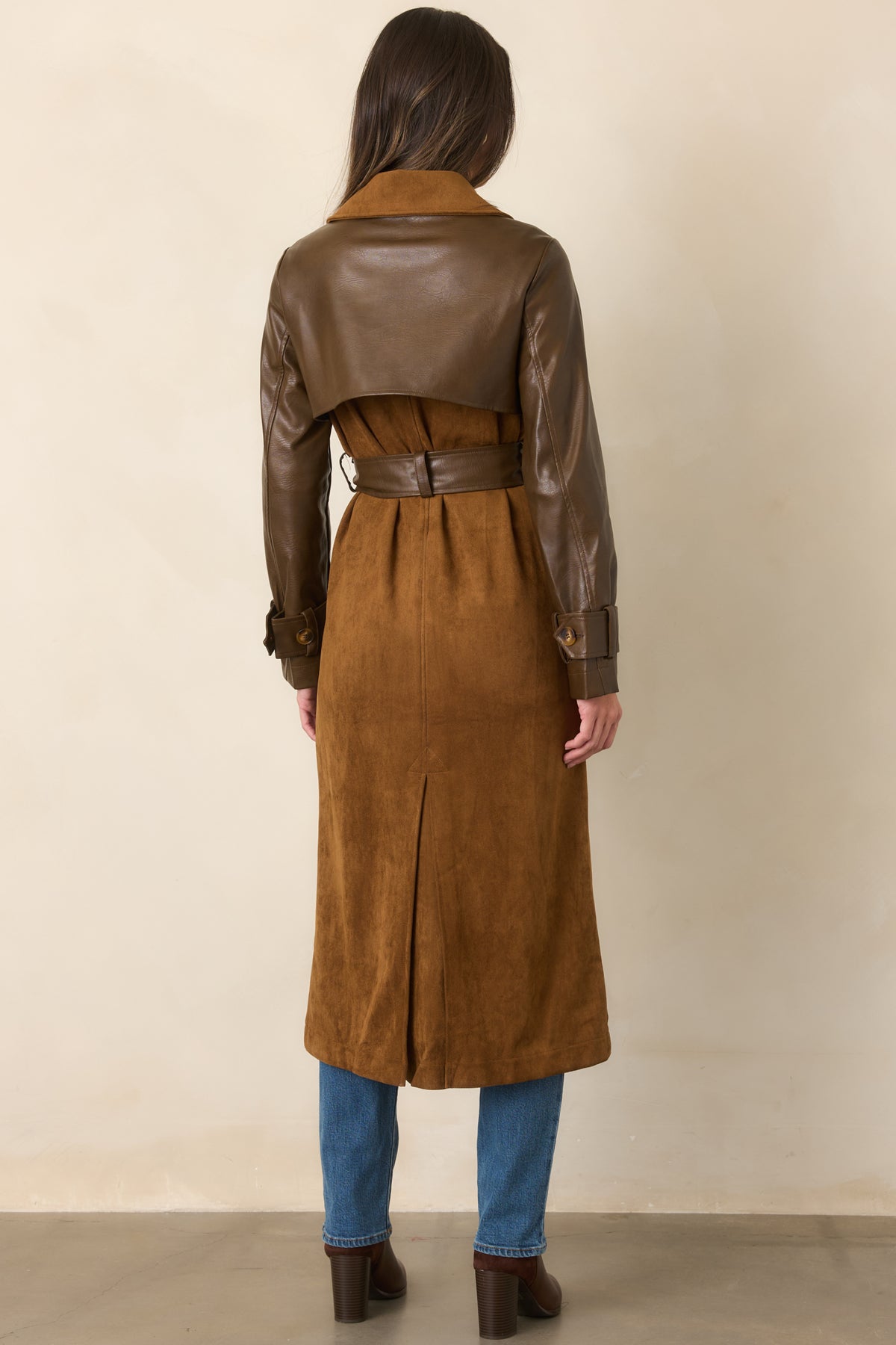 Rear of the caramel trench coat showing its long silhouette, smooth brown faux leather sleeves, and clean waistline.