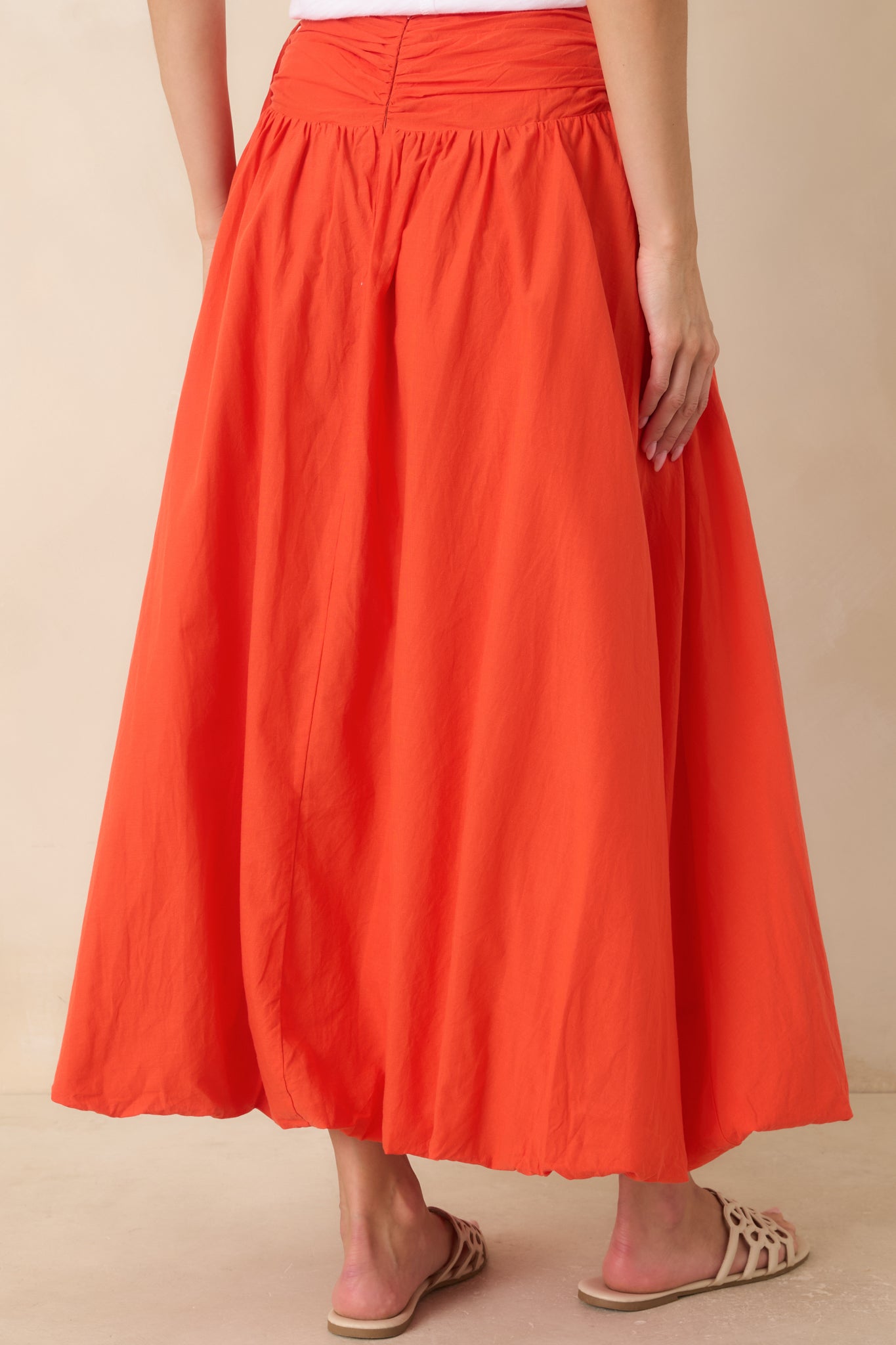 Rear view of the coral orange cotton maxi skirt highlighting the wide gathered waistband and full flowing silhouette.