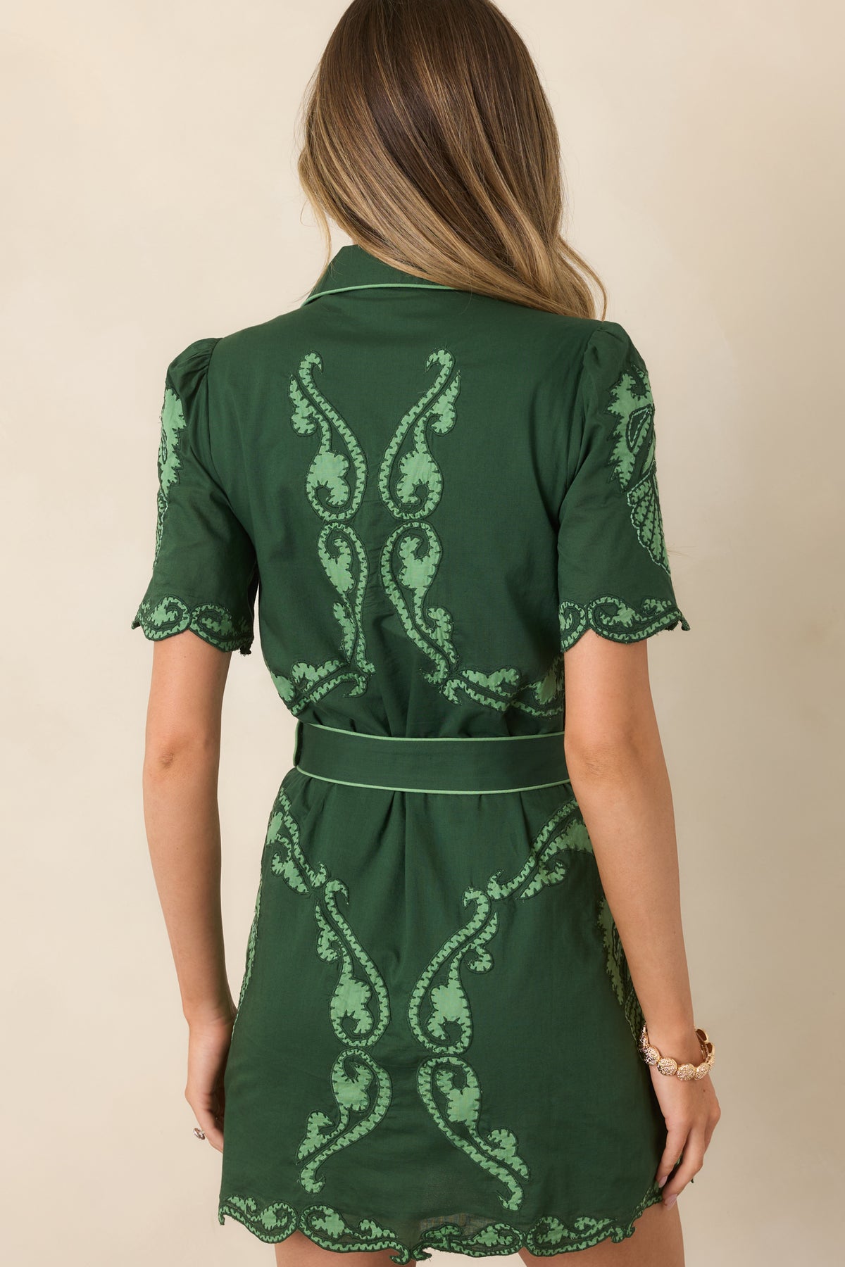 Rear of the deep green mini dress showing the gently flared skirt and scalloped hem.