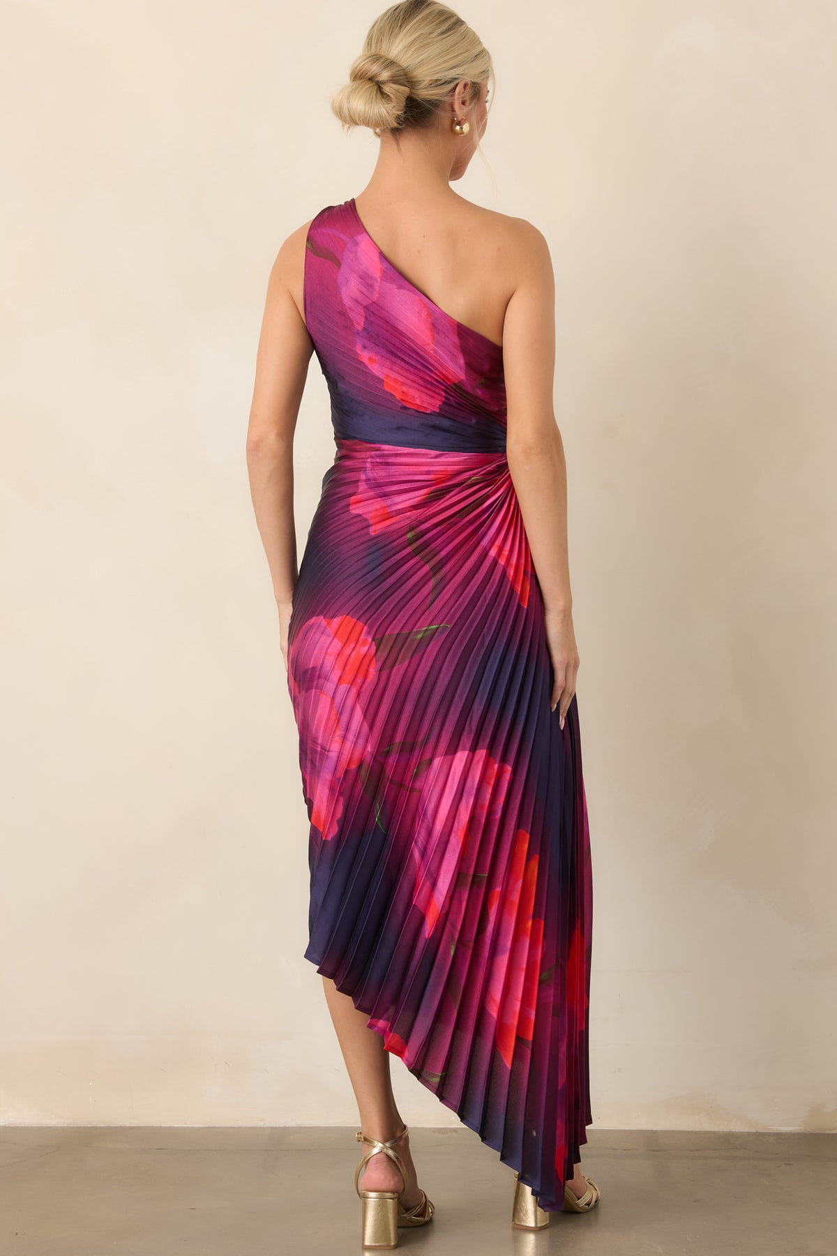Rear view shows the floral print continuing across the pleated silhouette, with the asymmetrical hem creating fluid movement.