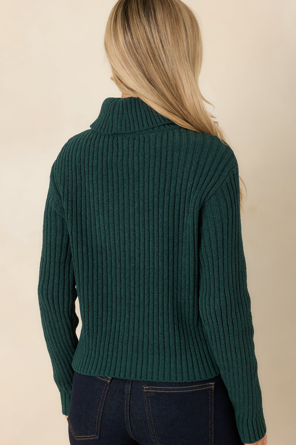 Rear view of the hunter green sweater featuring a folded turtleneck, dropped shoulders, and vertical ribbing throughout.