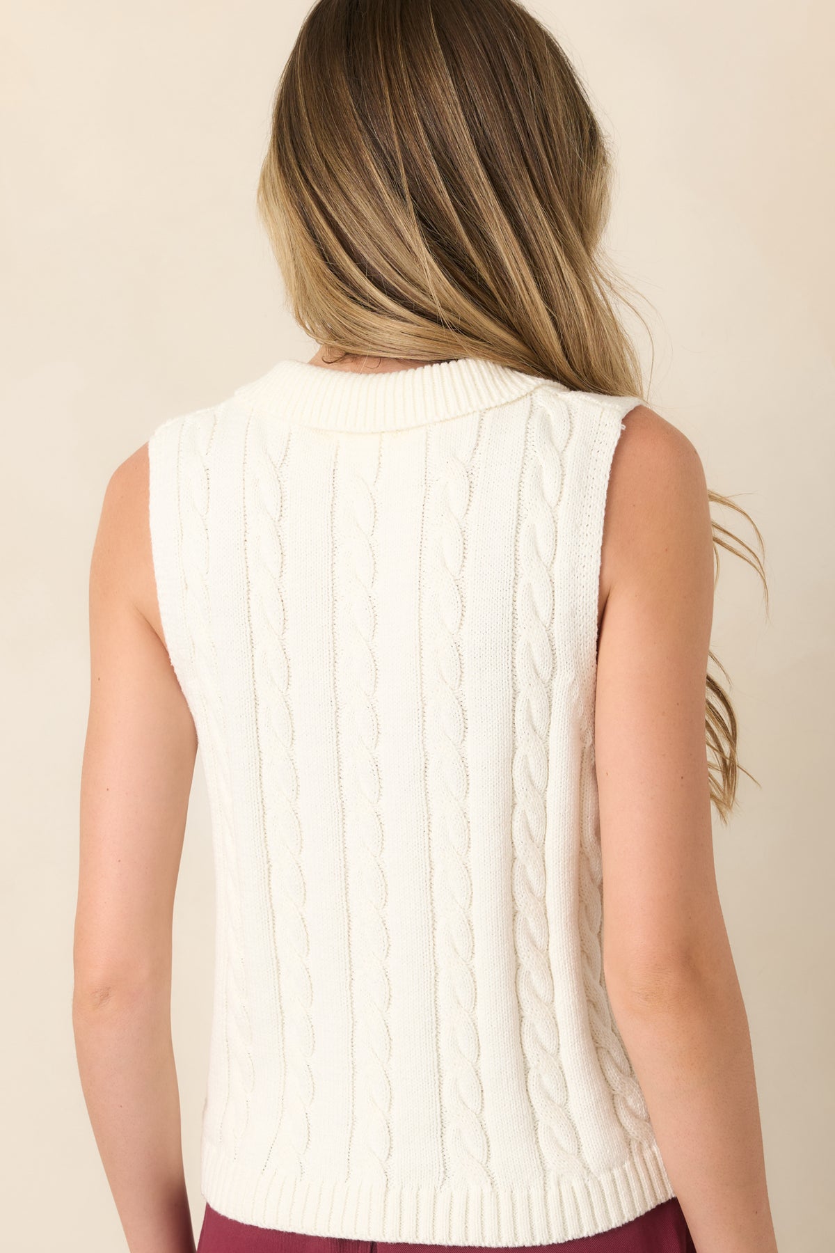 Rear view of the ivory cable-knit sweater vest featuring a sleeveless silhouette, textured knit construction, and wide ribbed hem.