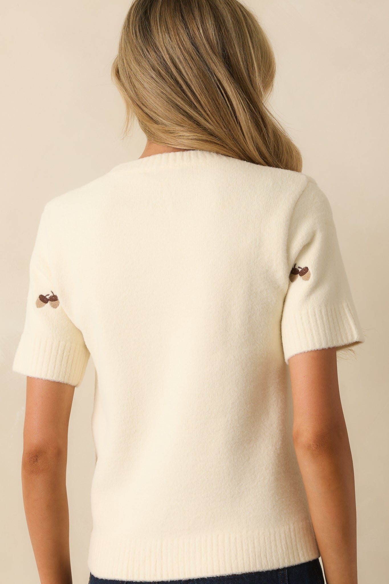 Rear view of the ivory sweater with embroidered motifs and ribbed hem finishing.