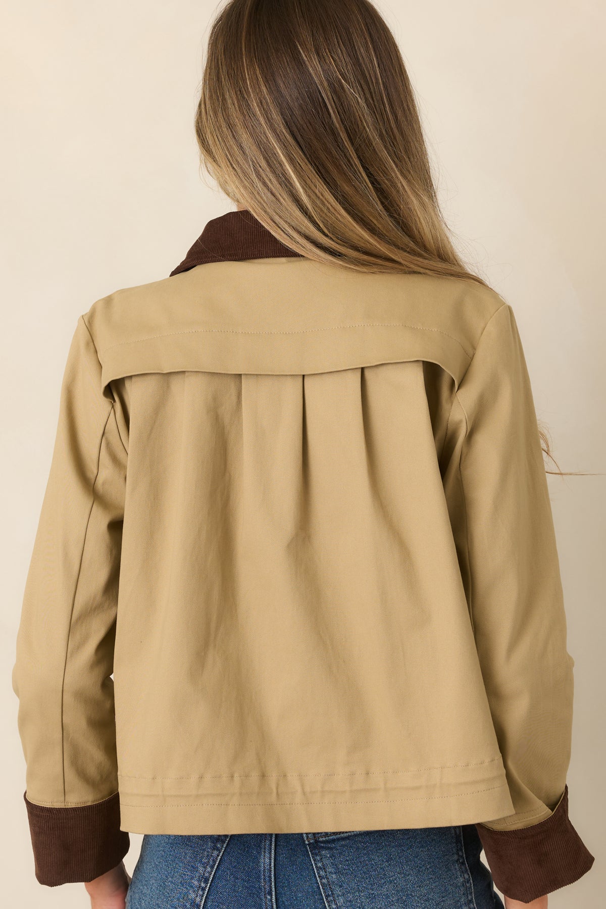 Rear of the khaki jacket showing dimensional pleating across the back and the contrasting brown collar.
