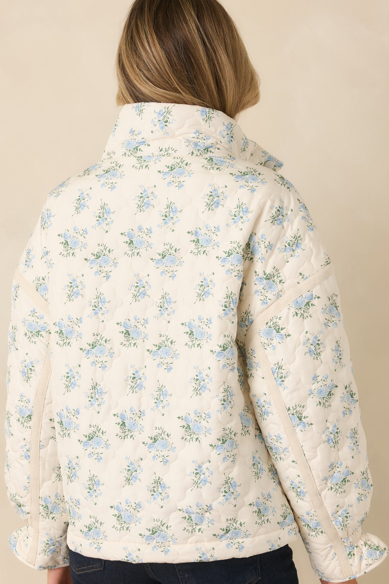 Rear of the ivory quilted jacket showing continuous floral quilting, long sleeves, and smooth back panel with light padding.