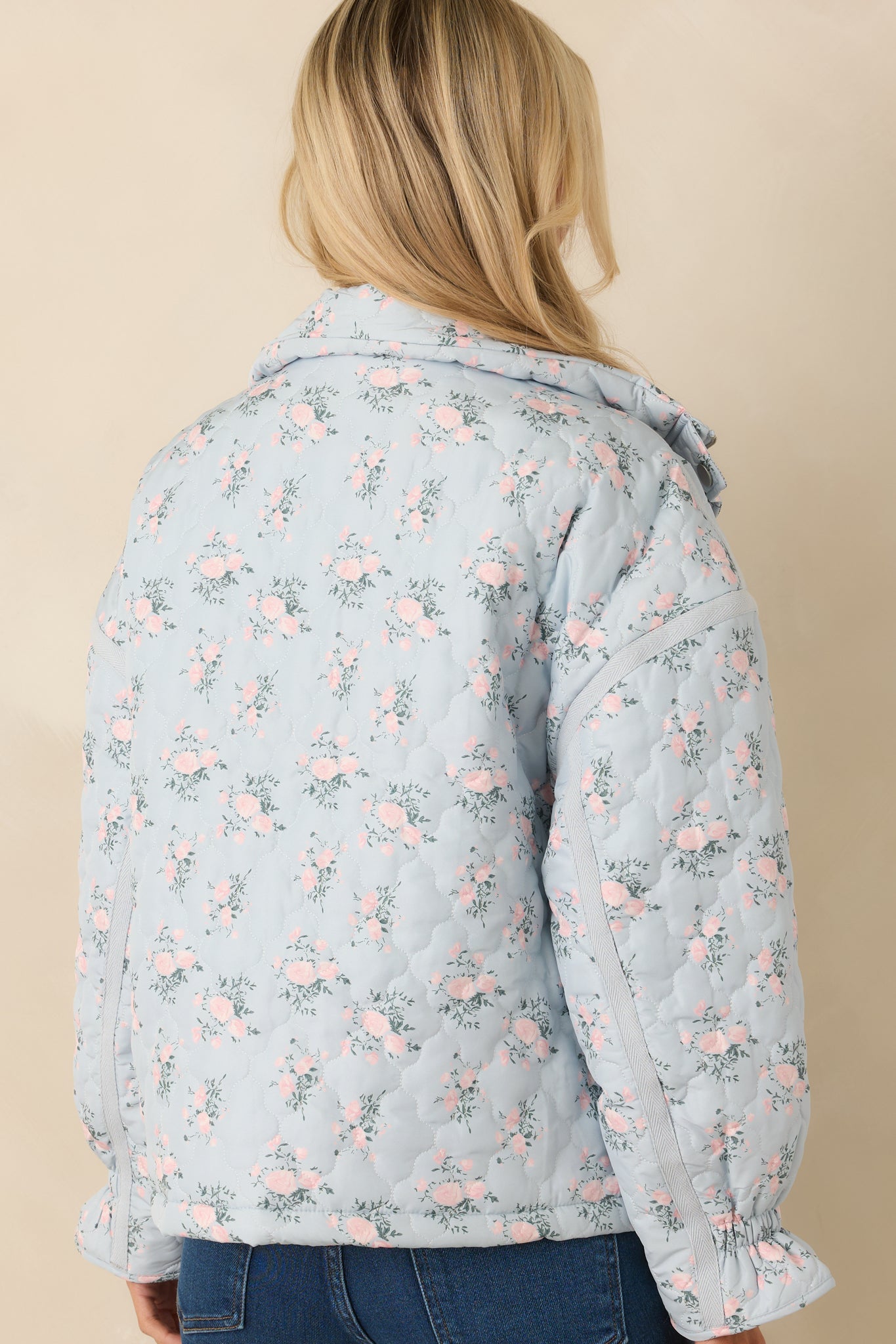 Rear of the light blue quilted jacket showing continuous floral quilted pattern, smooth back panel, and long sleeves with elastic cuffs.