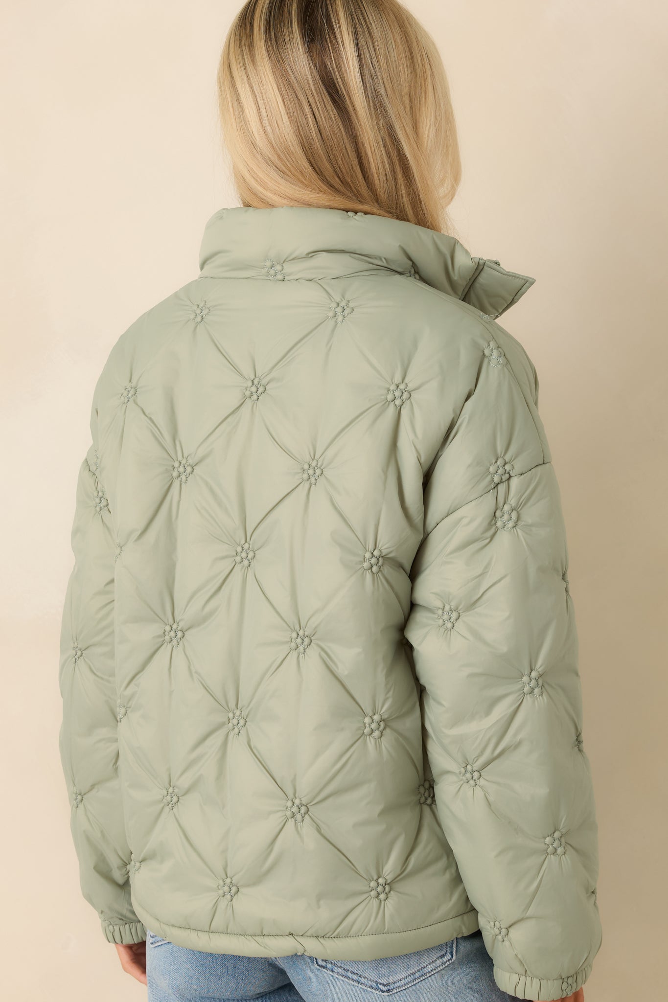 Rear of the sage green puffer jacket showing continuous floral-inspired quilting, long sleeves, and straight hemline.