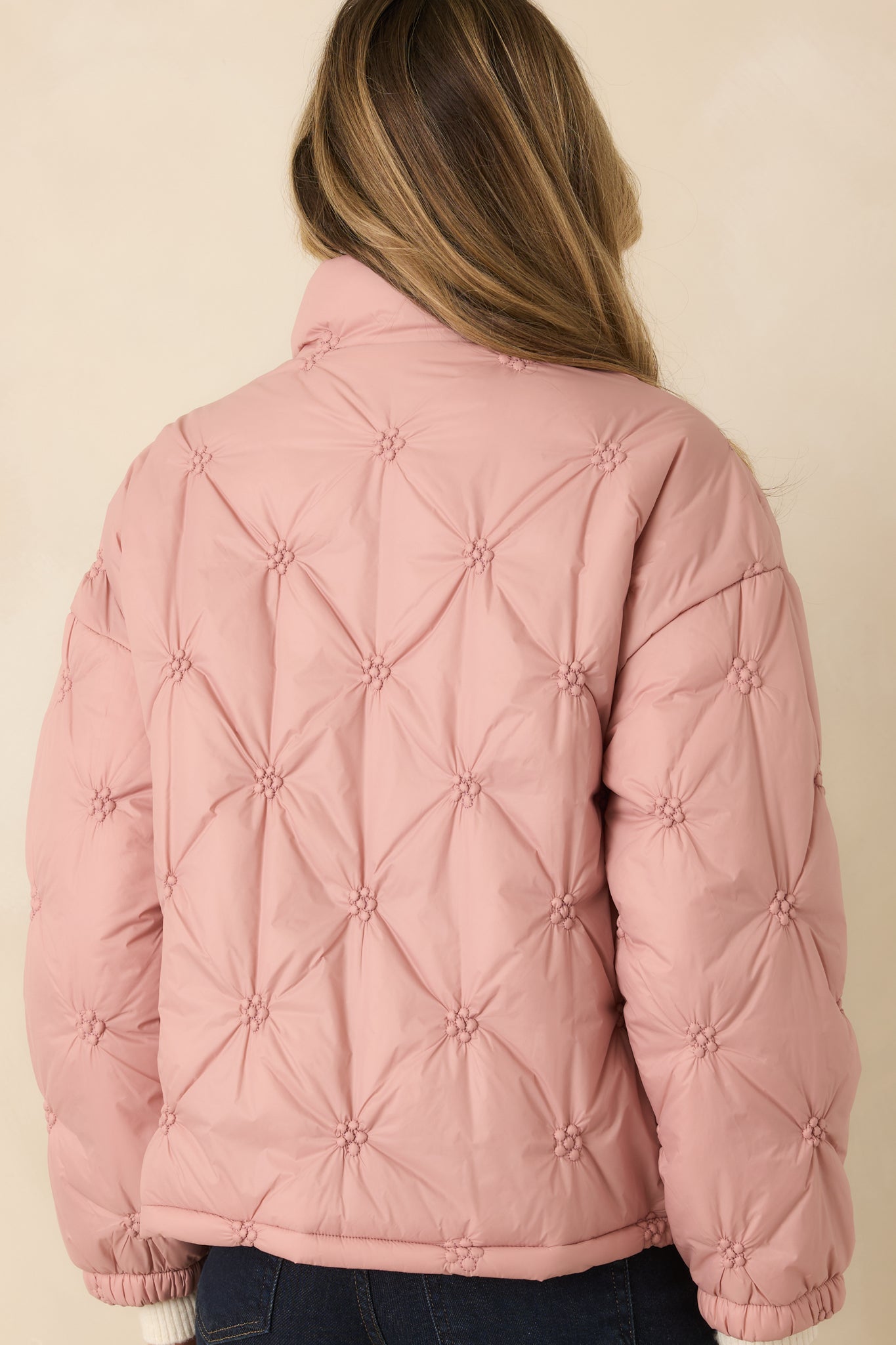 Rear of the blush pink puffer jacket showing continuous floral-inspired quilted pattern, long sleeves, and straight hemline.