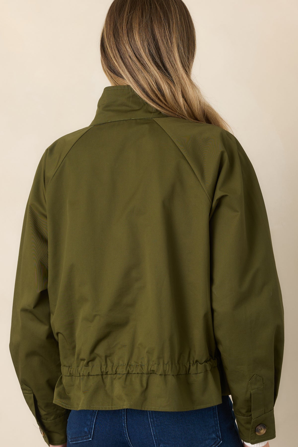 Rear of the olive cotton jacket showing the adjustable drawstring waist and softly ruffled hem.