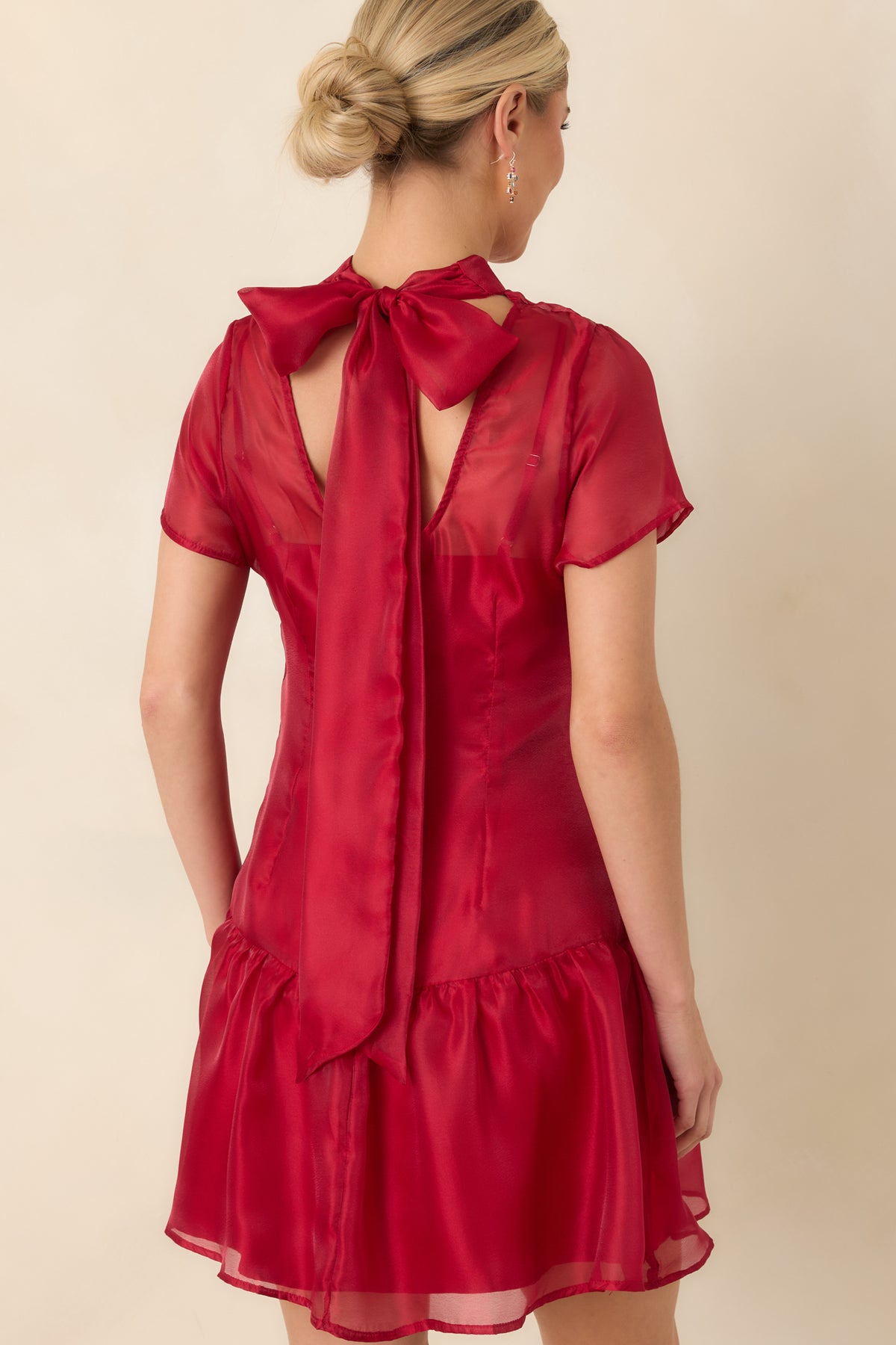 Rear view of the red mini dress featuring an open back, oversized neckline bow, long trailing ties, and gathered ruffle hem.