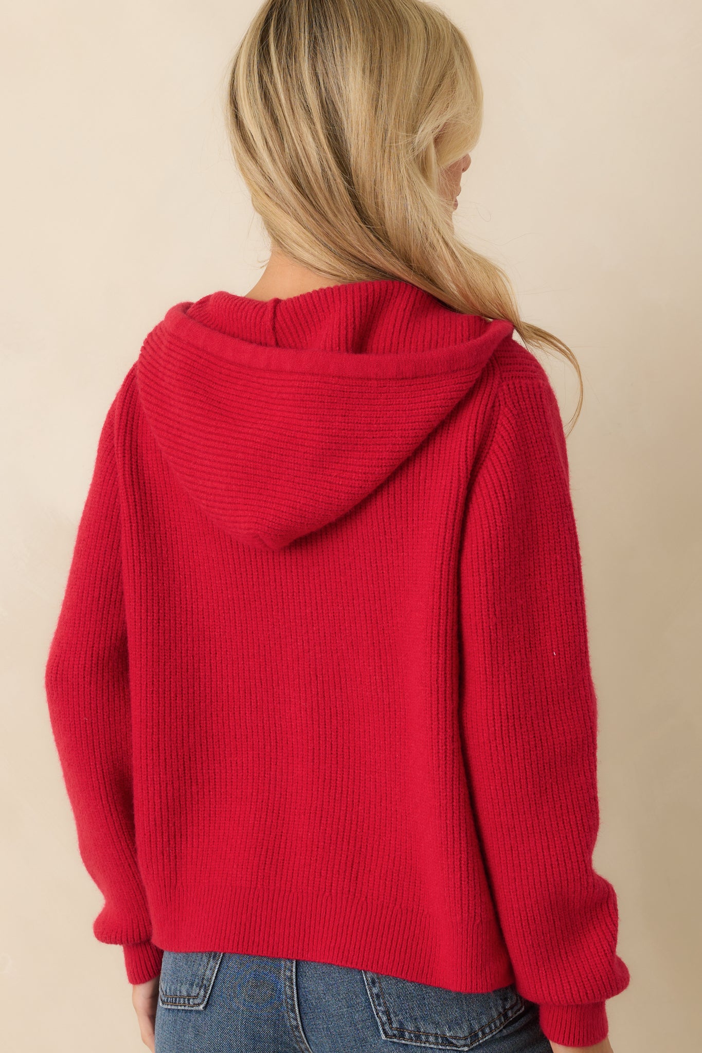 Rear view of the red ribbed knit jacket showing long sleeves, drawstring hoodie, and ribbed hemline.