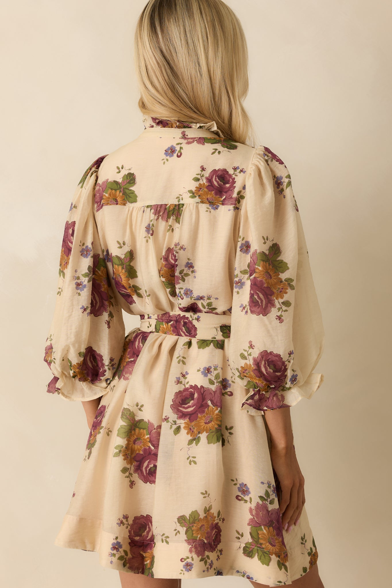 Rear view of the beige floral mini dress showing the puff sleeves, self-tie waist, and relaxed fit silhouette.