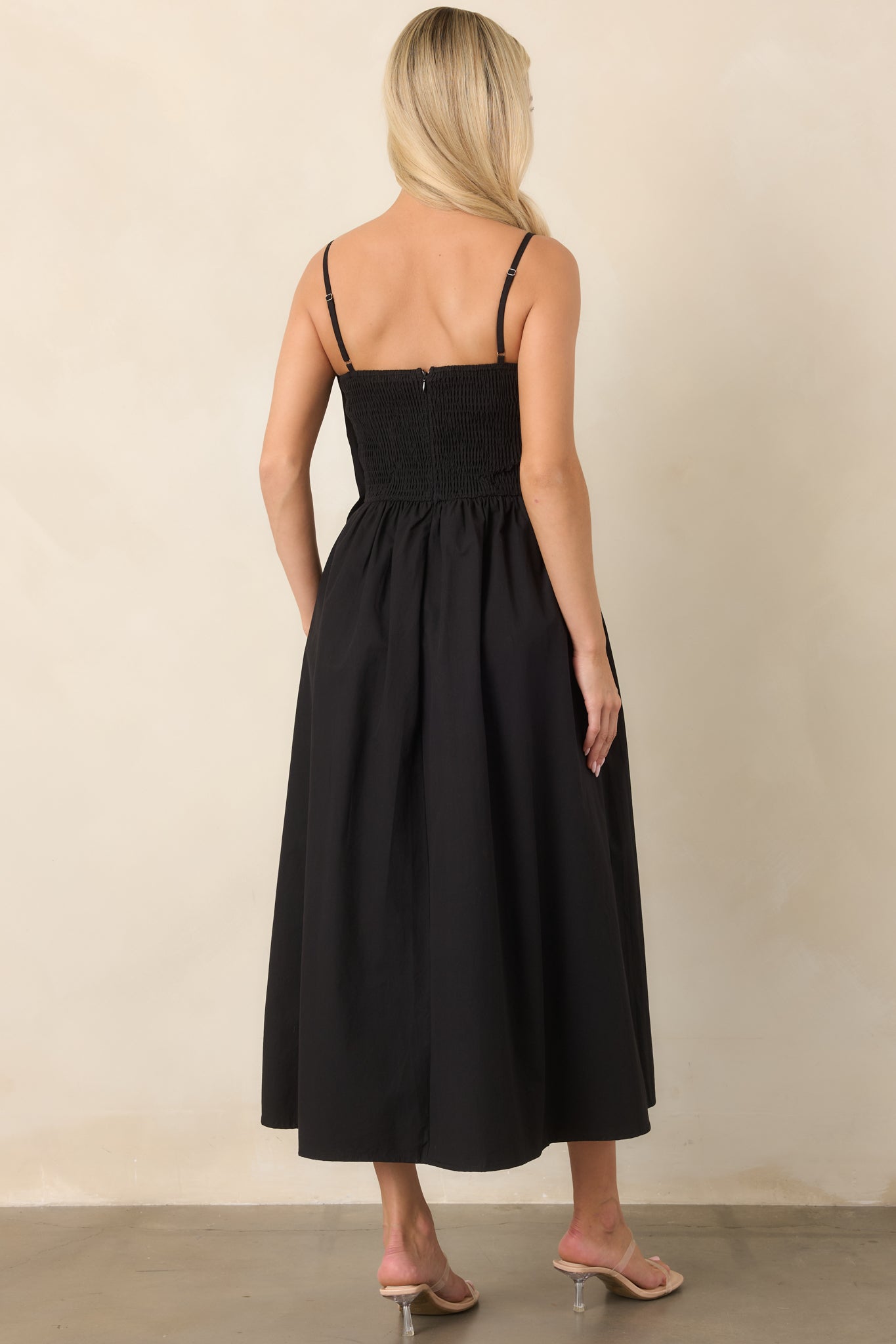 Rear view of the black cotton midi dress showing its flexible smocked back, adjustable straps, gathered waist, and full skirt.