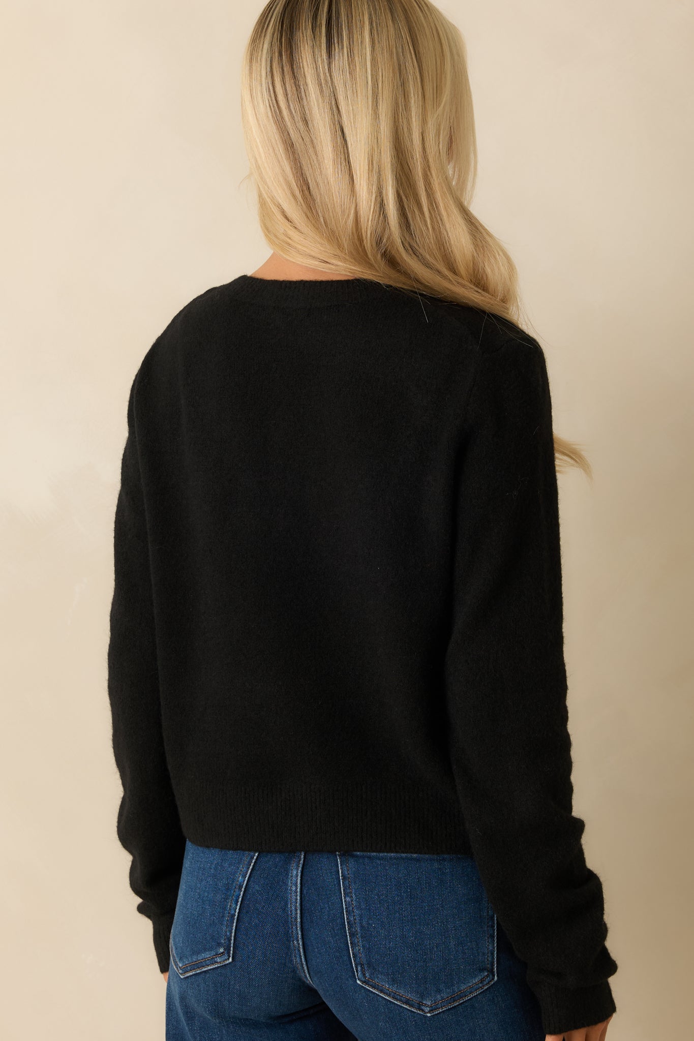 Rear view of the black knit cardigan showing its relaxed shape and ribbed trim along the hem.