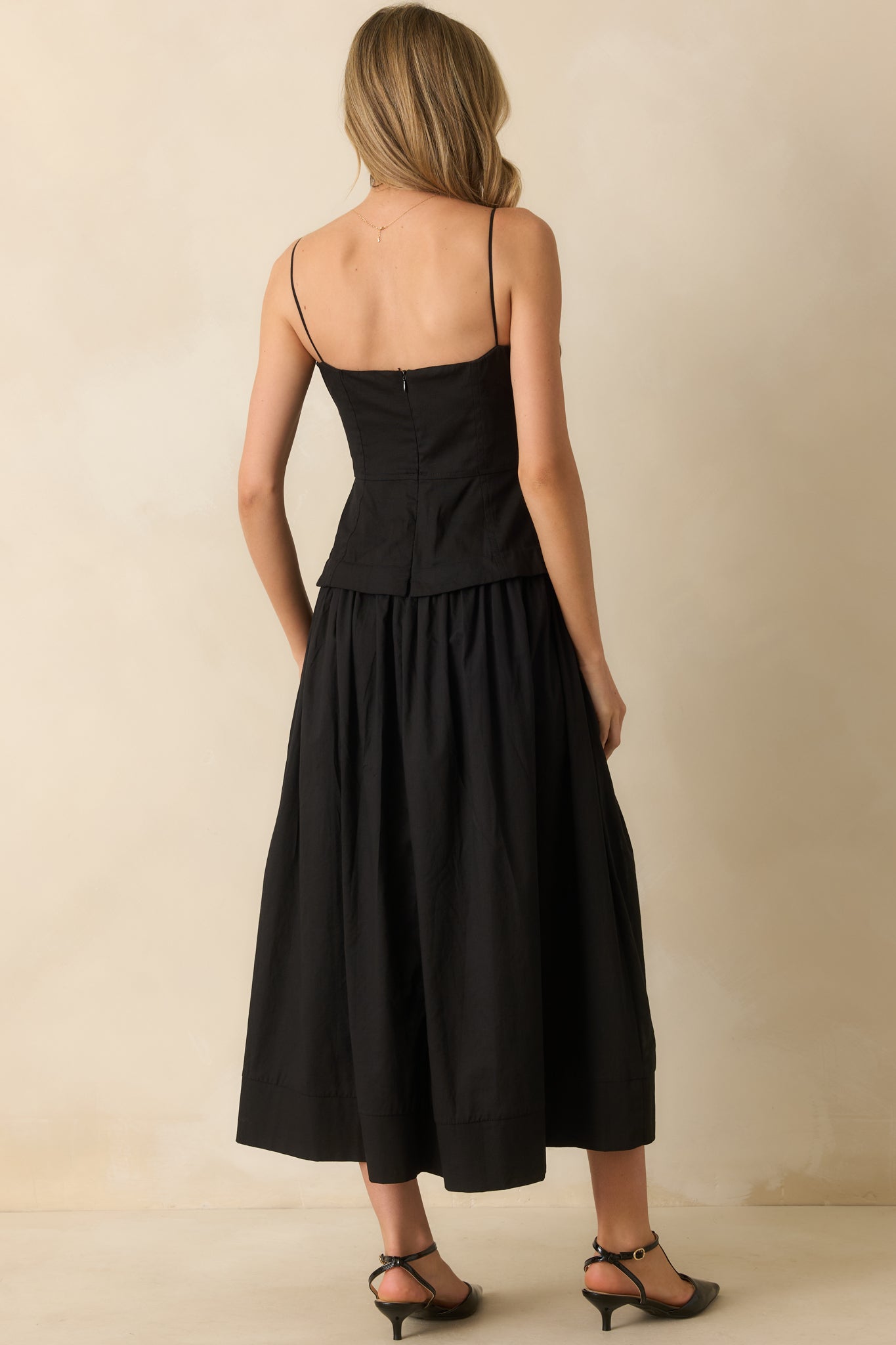 Rear view of the black midi dress showing the concealed zipper, adjustable straps, and gently gathered skirt.