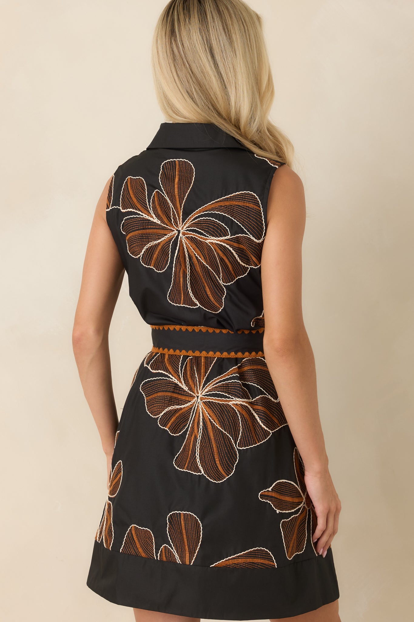 Rear view of the black mini dress showcasing the sleeveless A-line silhouette, tailored shape, and embroidered floral detailing.