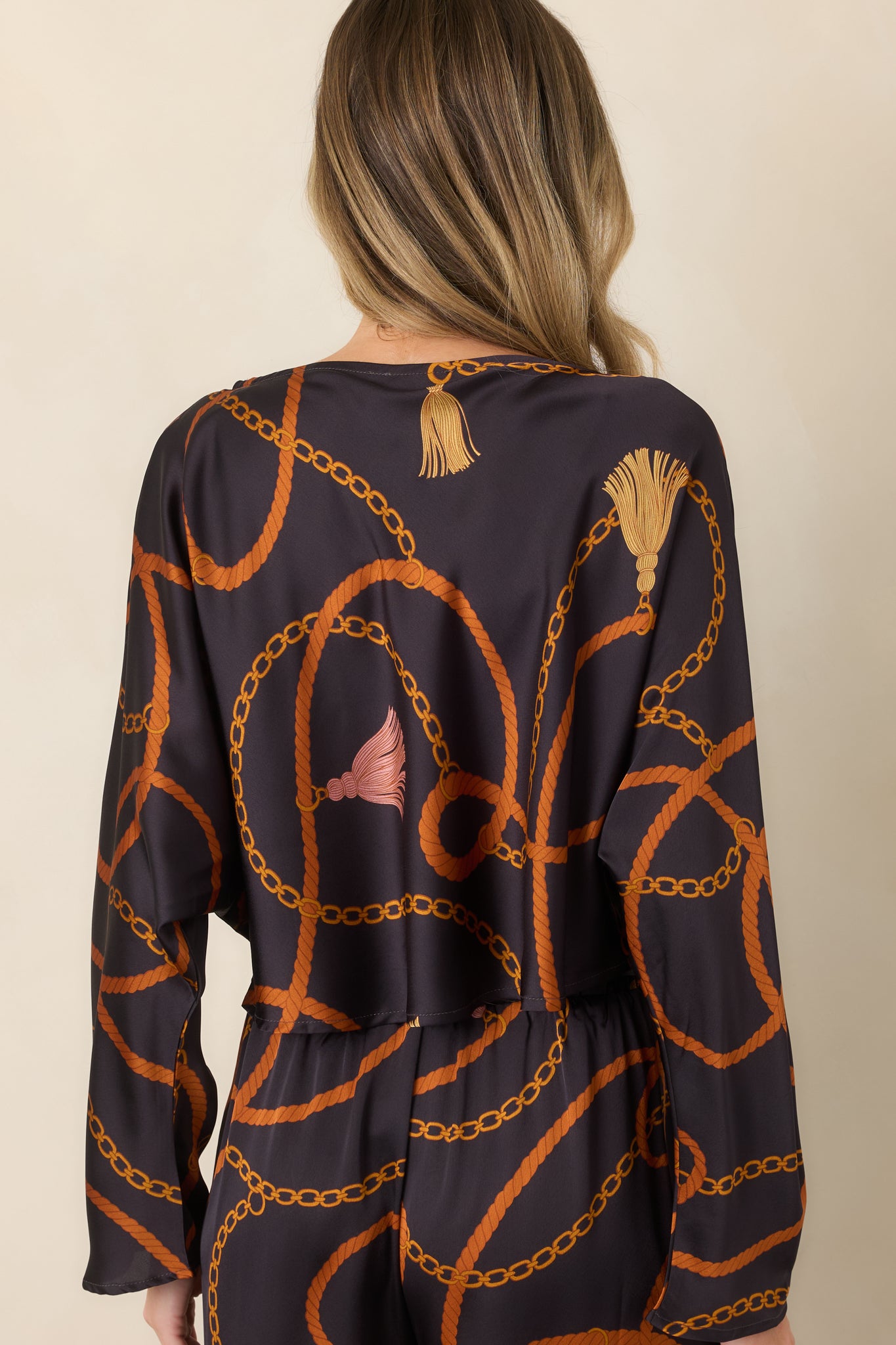 Rear view of the black satin-feel top showcasing its relaxed cropped silhouette, long sleeves, and decorative print.