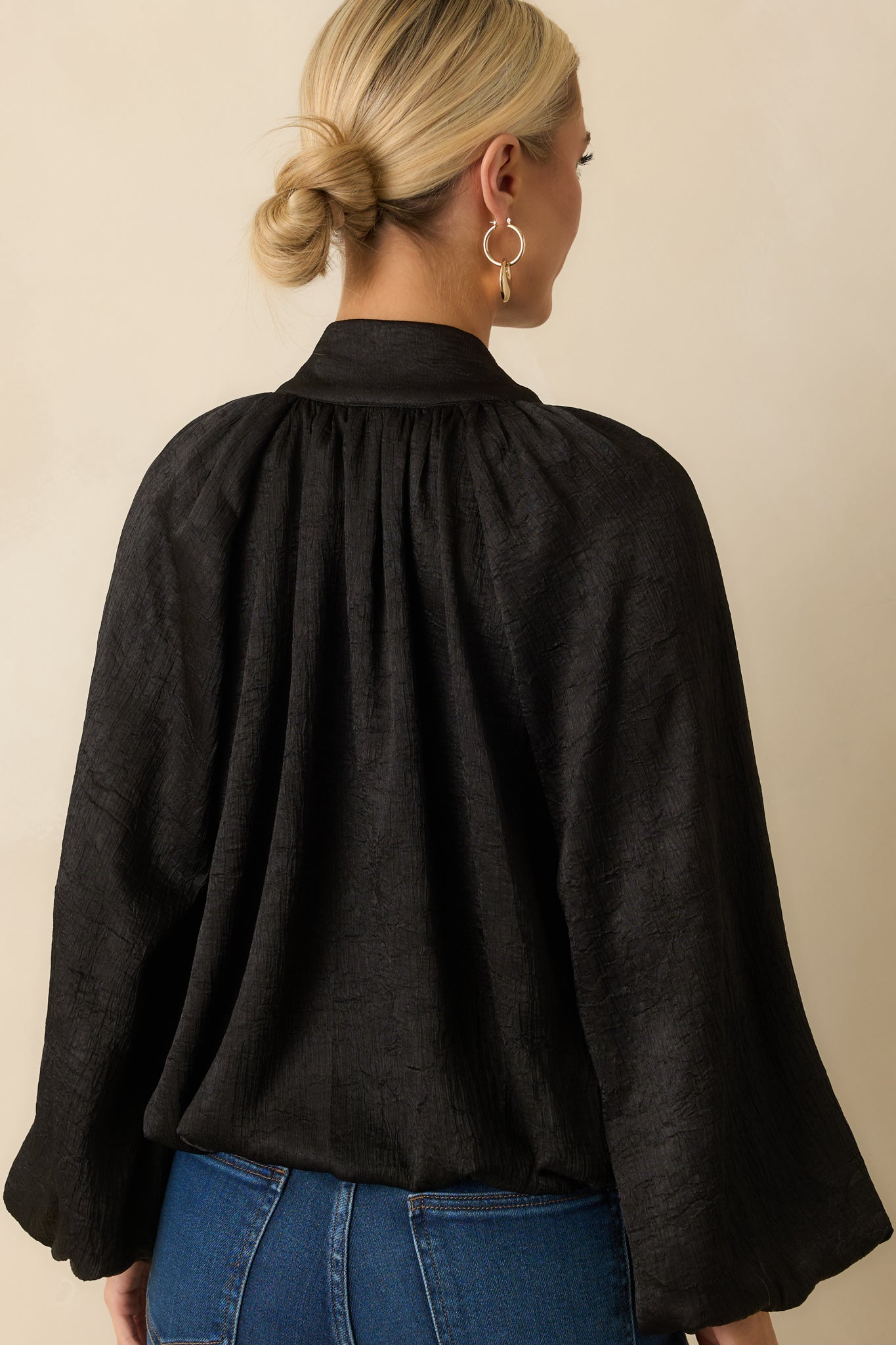 Rear view of the black satin V-neck top highlighting the relaxed silhouette and long peasant sleeves.